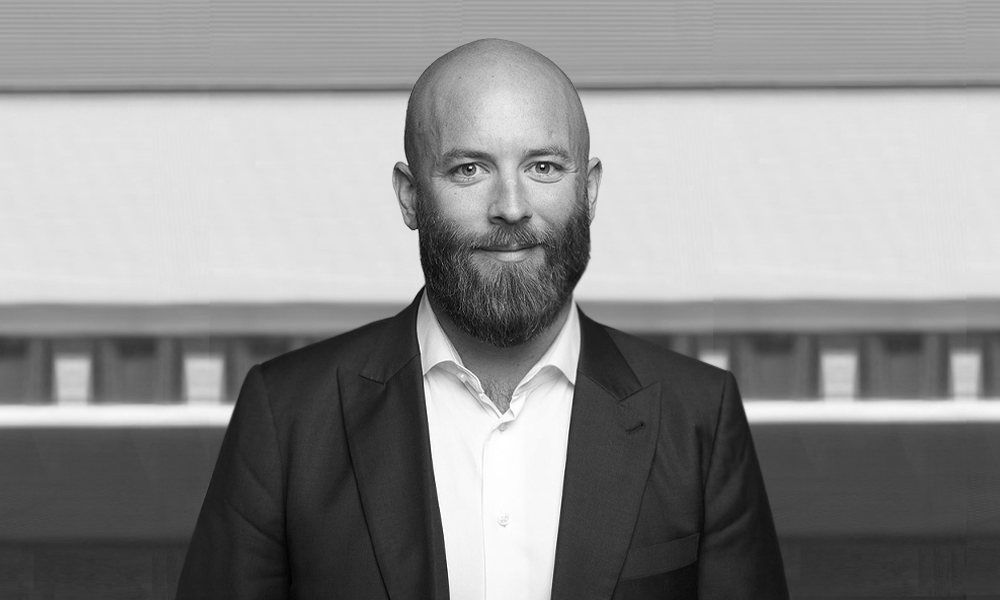 A man with a beard is wearing a suit and smiling in a black and white photo.