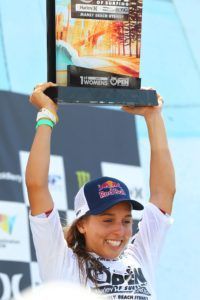 A woman in a red bull hat is holding a trophy over her head.