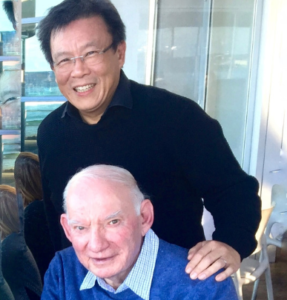 A man in a black sweater is standing next to an older man in a blue sweater