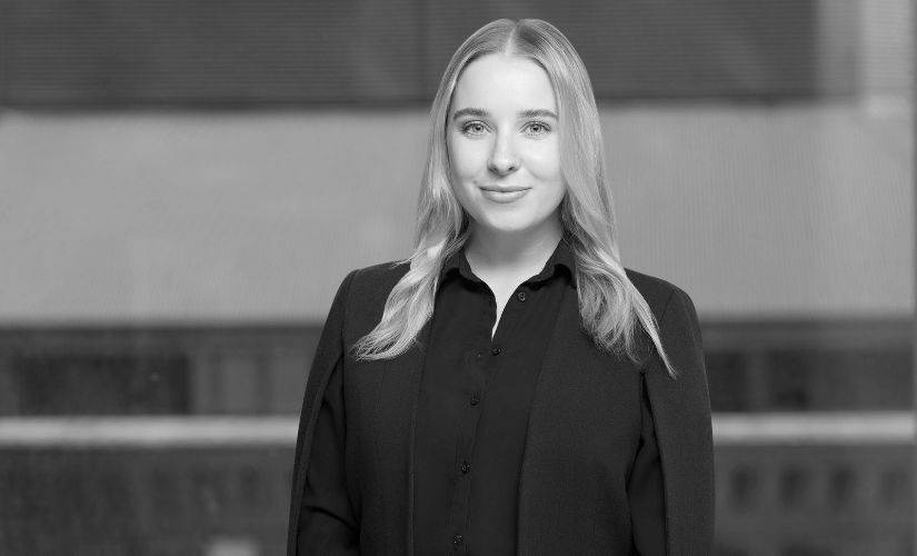 A black and white photo of a woman in a black shirt standing in front of a building.