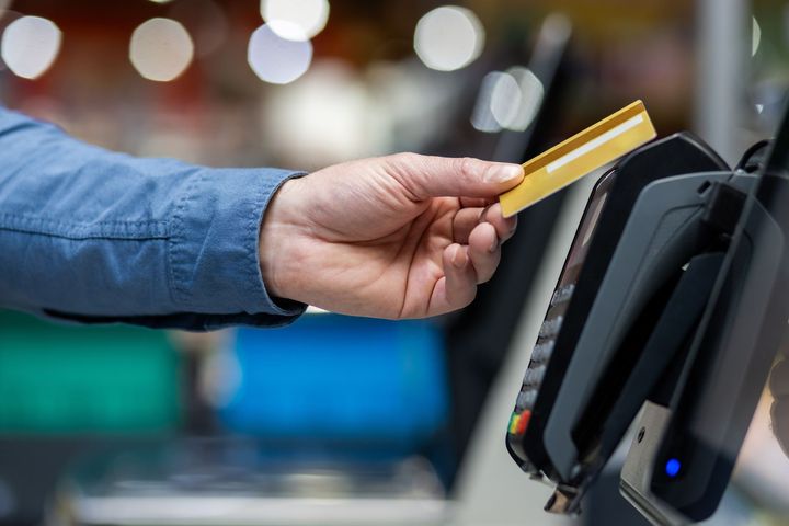 Hand holding a yellow credit card near a payment terminal at a checkout counter