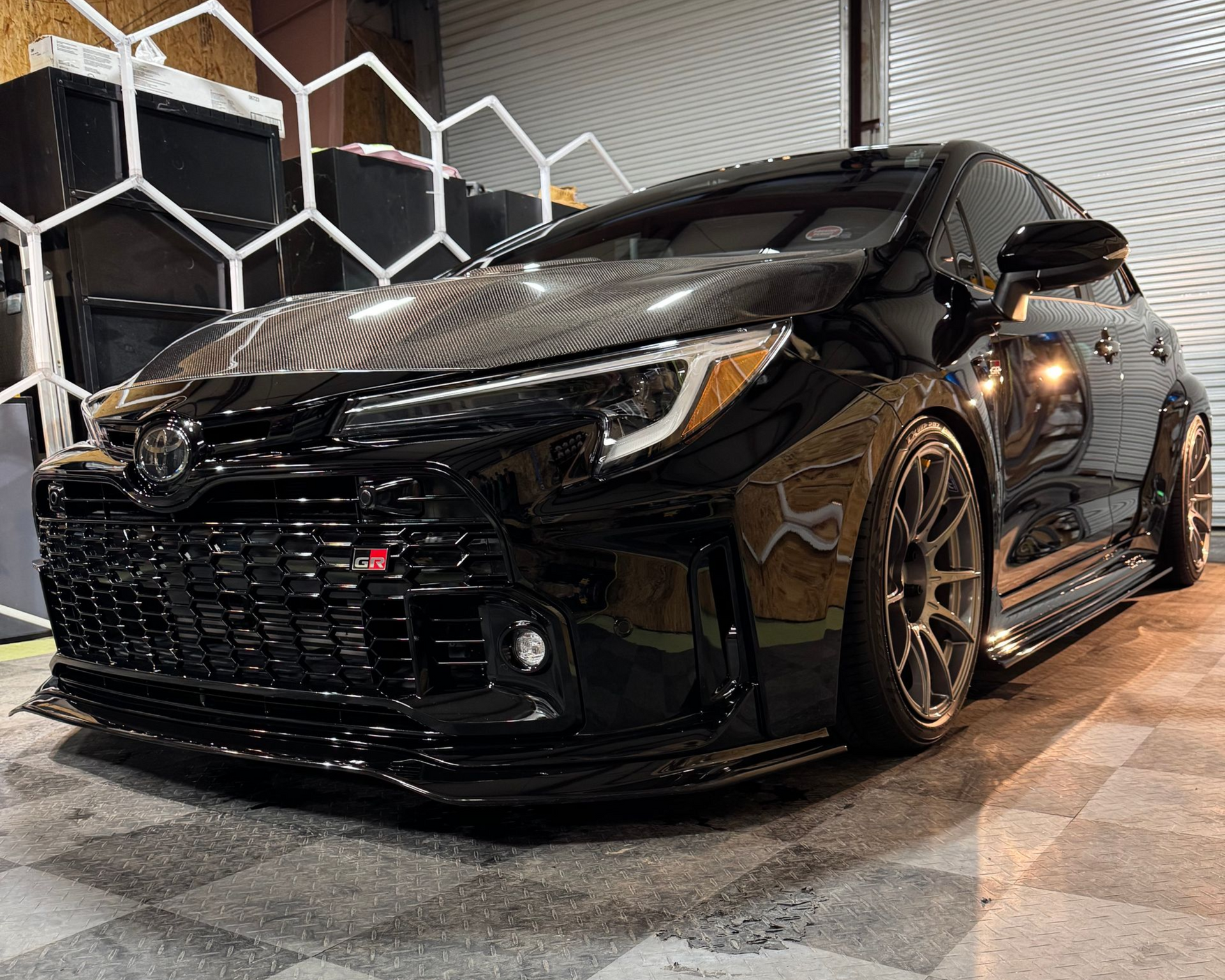 Black Toyota GR Corolla with carbon fiber hood, front lip, and aftermarket wheels.