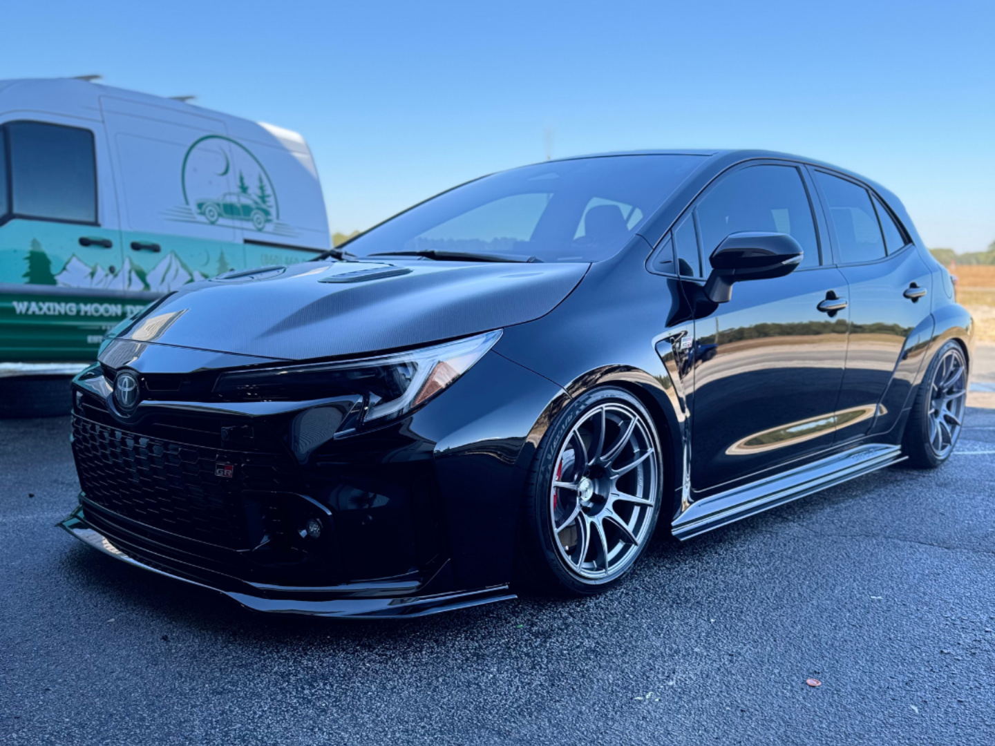 Black Toyota Corolla hatchback parked, lowered suspension, gray wheels, front lip.