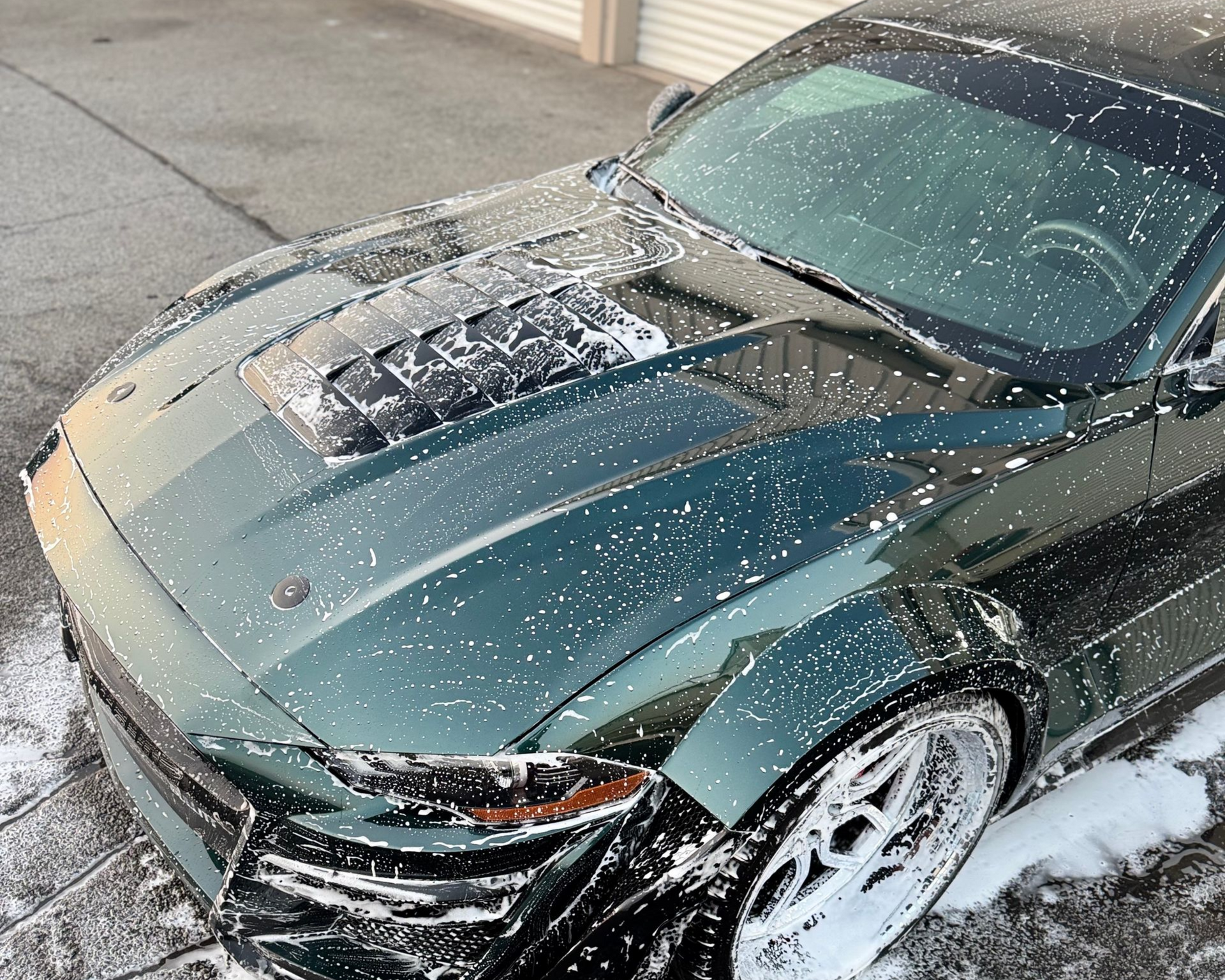Green Ford Mustang covered in soap suds, being washed.