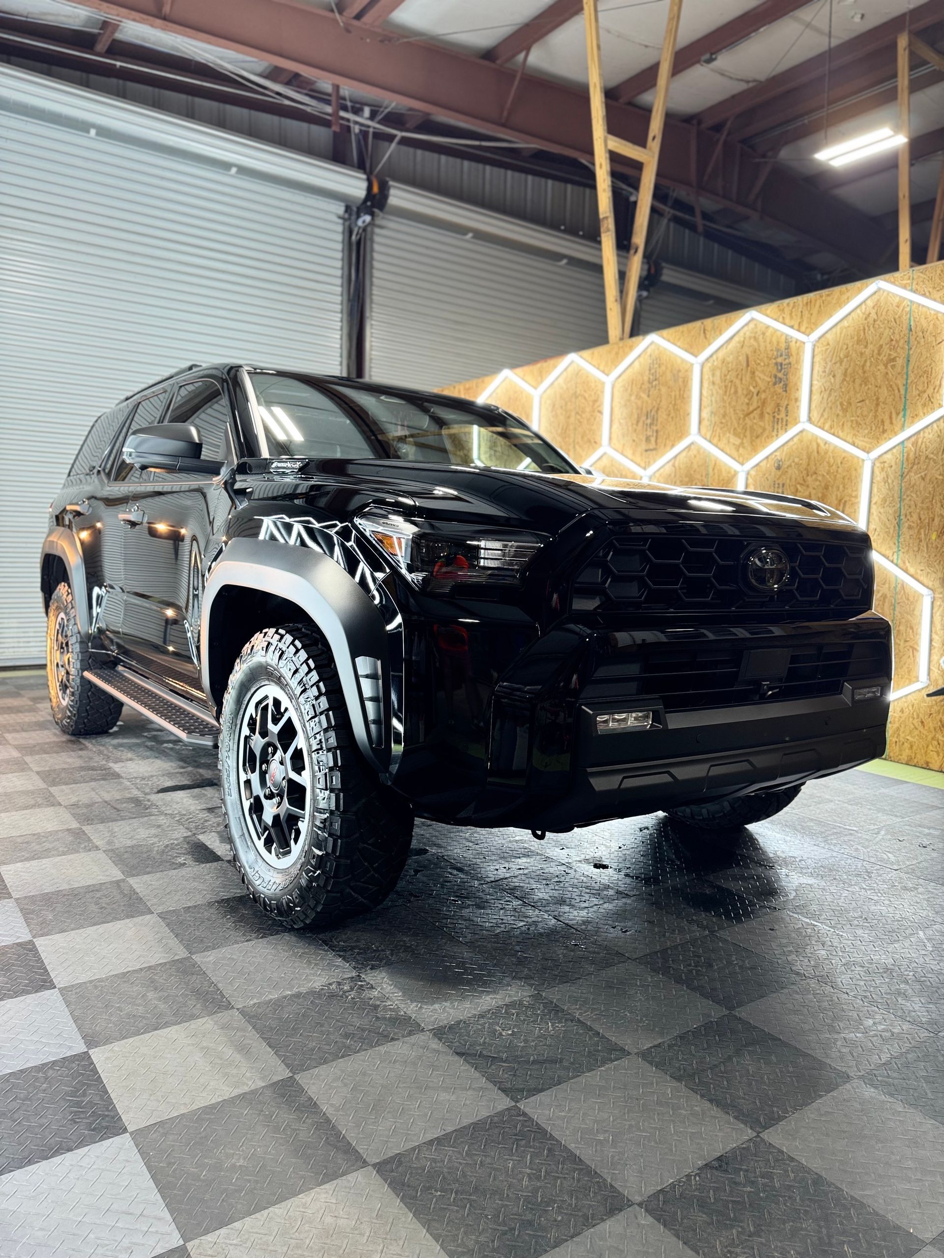 Black SUV parked on a tiled floor inside a garage, next to a honeycomb-shaped light fixture.