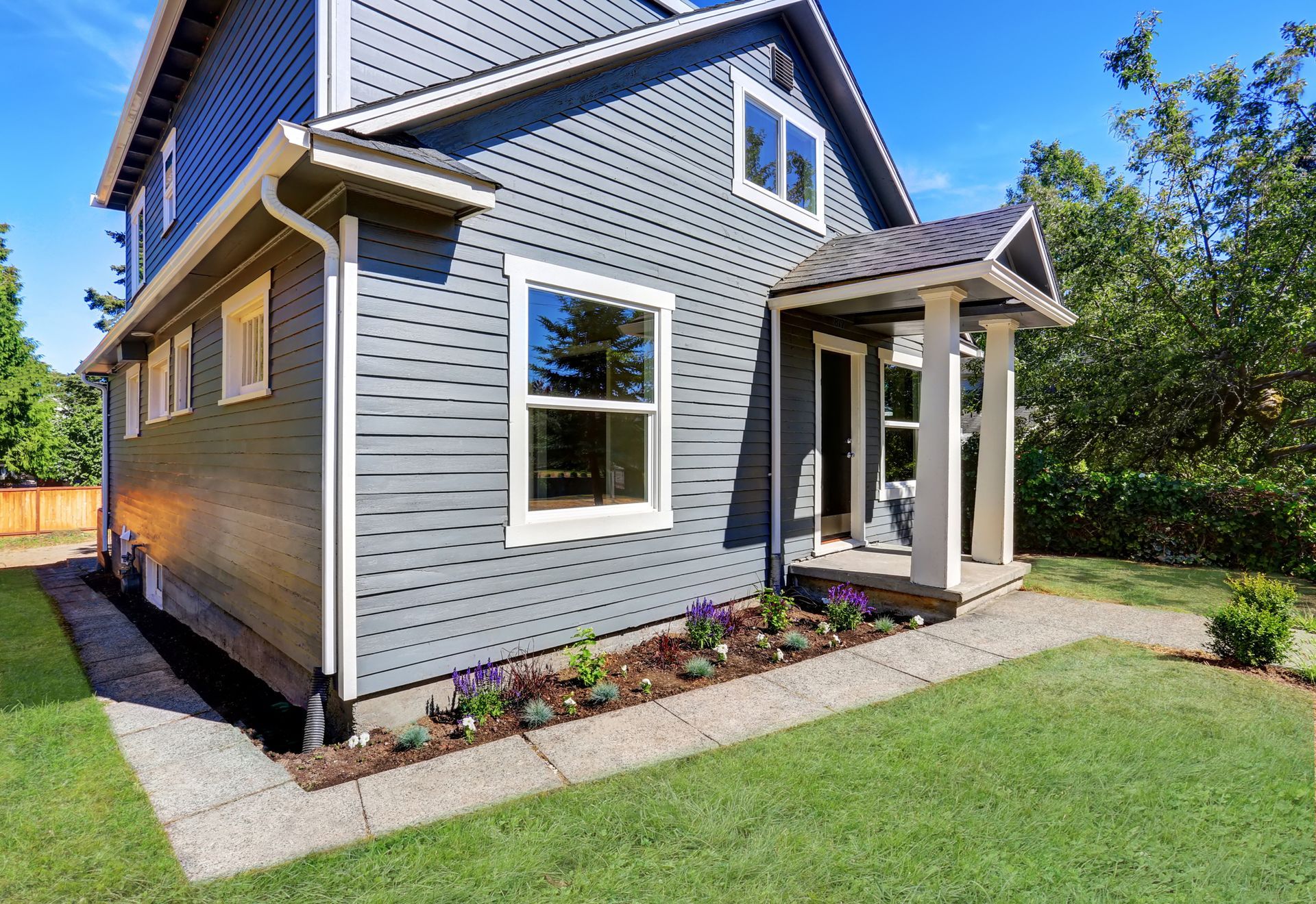 A large gray house with a porch and a walkway in front of it.