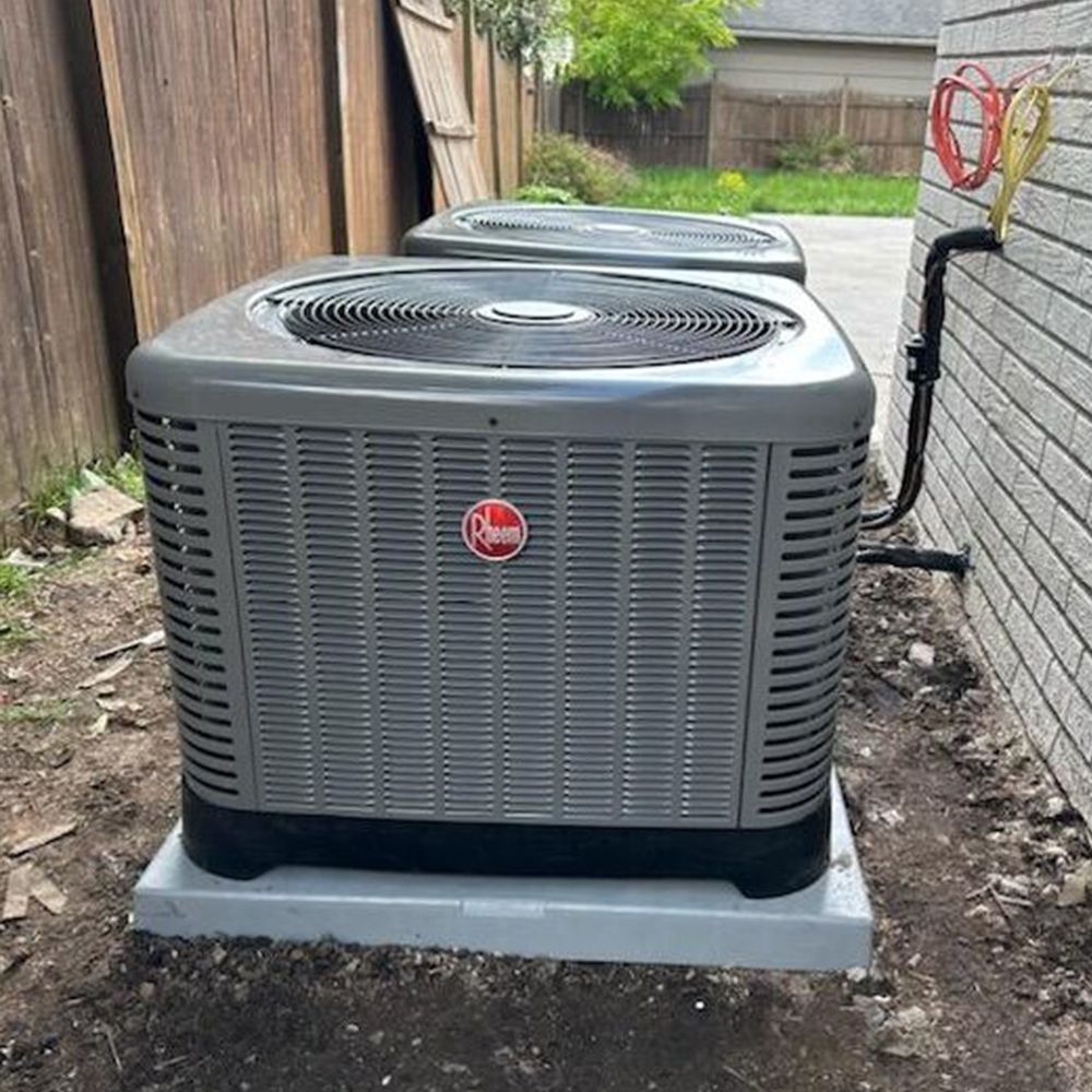 Two air conditioners are sitting next to each other on the side of a house.