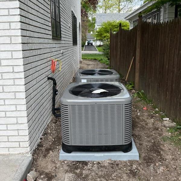 Two air conditioners are sitting on the side of a brick building.