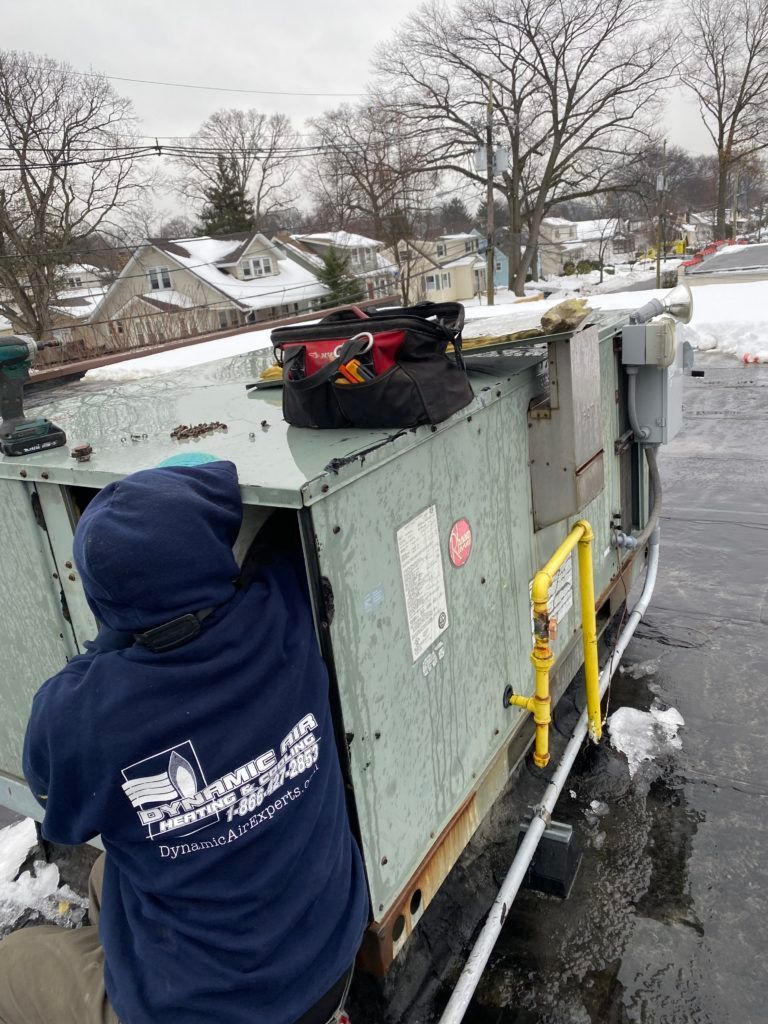 A man in a blue hoodie is working on an air conditioner on the roof of a building.