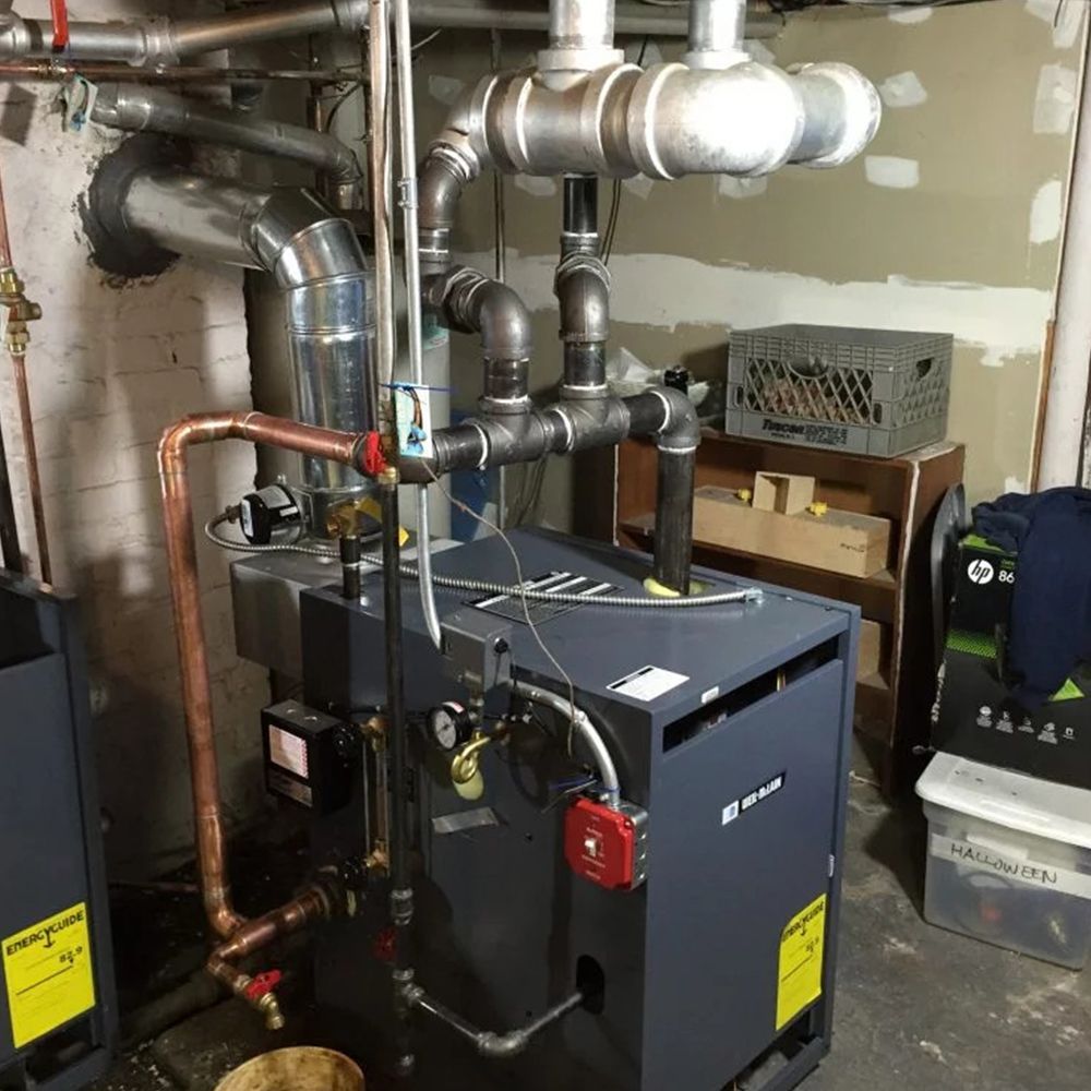 A boiler is sitting in a basement surrounded by pipes.