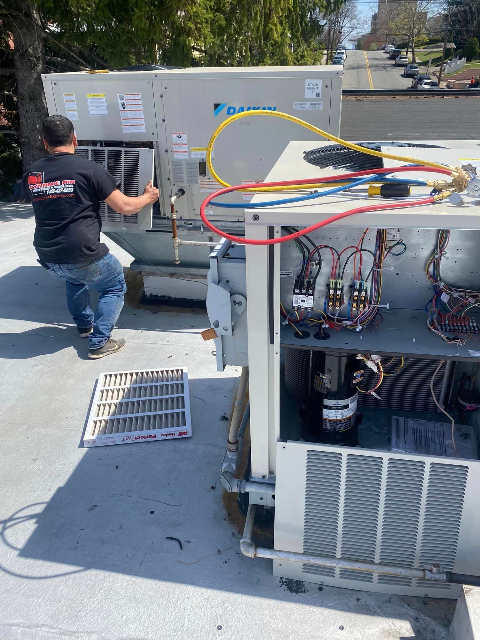 A man is working on an air conditioner on the roof of a building.