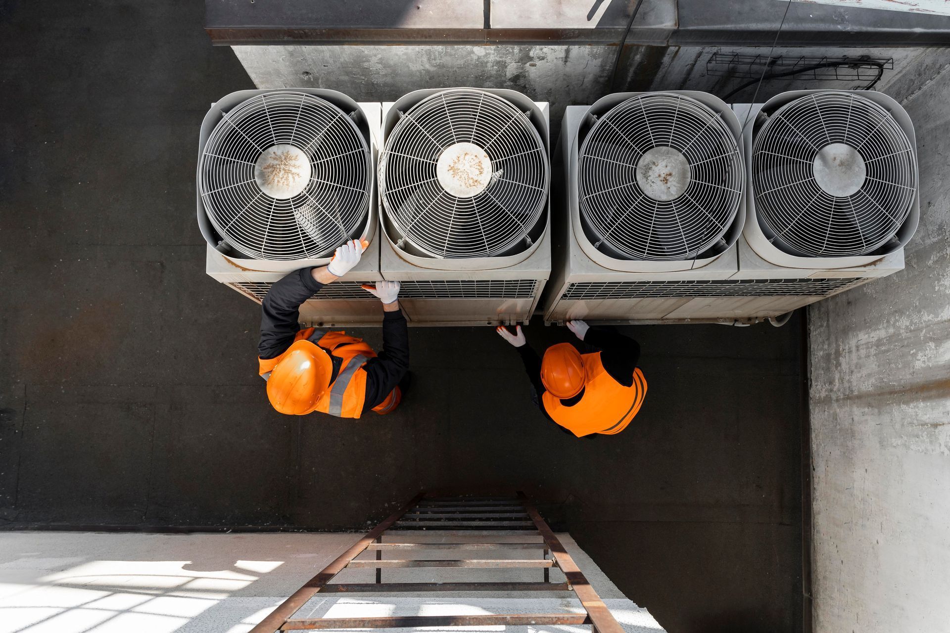 Two men are working on a ceiling fan in a building.