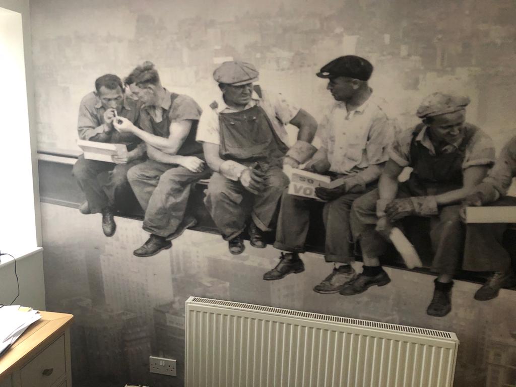 This is a picture of a wall which has been wallpapered using a Muriel theme of 5 work men sitting high up on a crane done by Painters and decorators Leicester