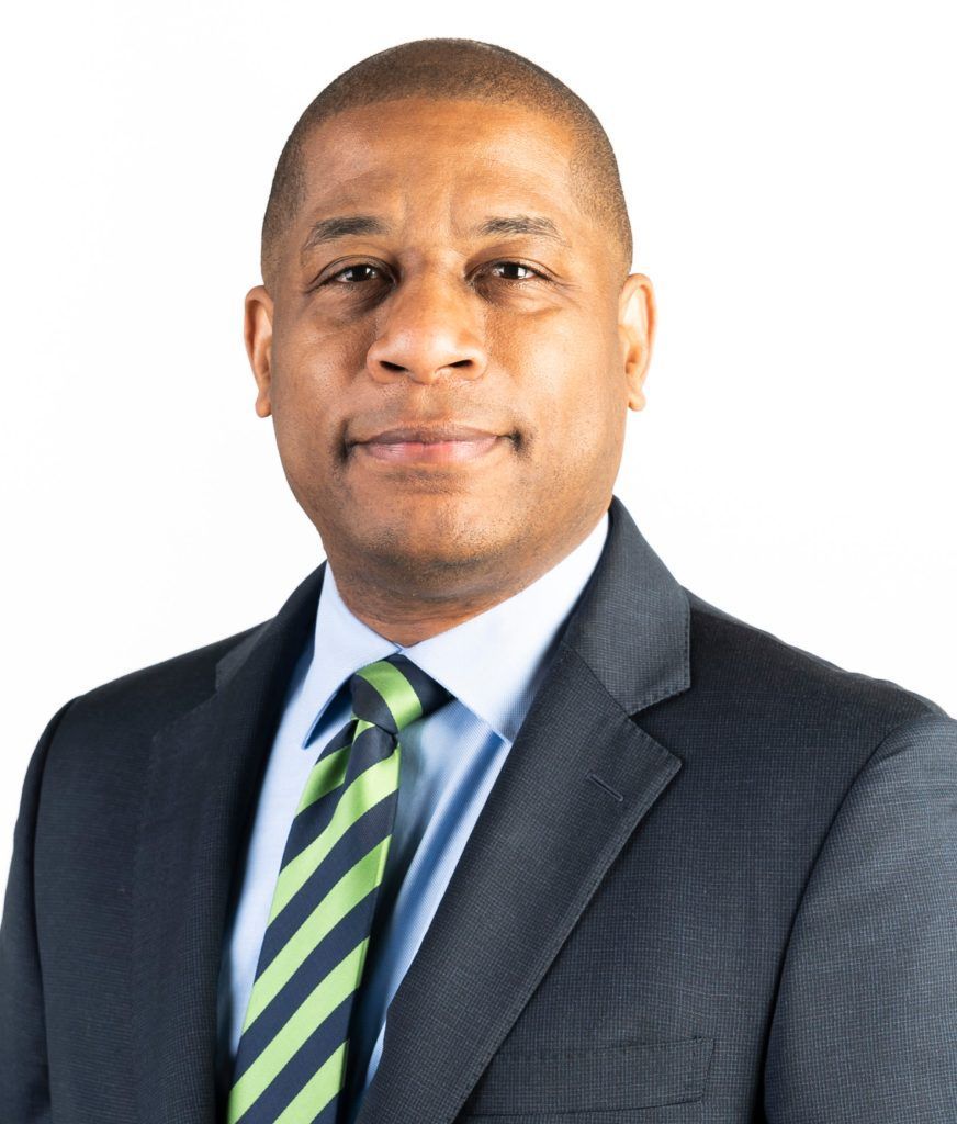 Headshot of a person in a navy blazer, light blue shirt, and green and navy striped tie, against a white background.