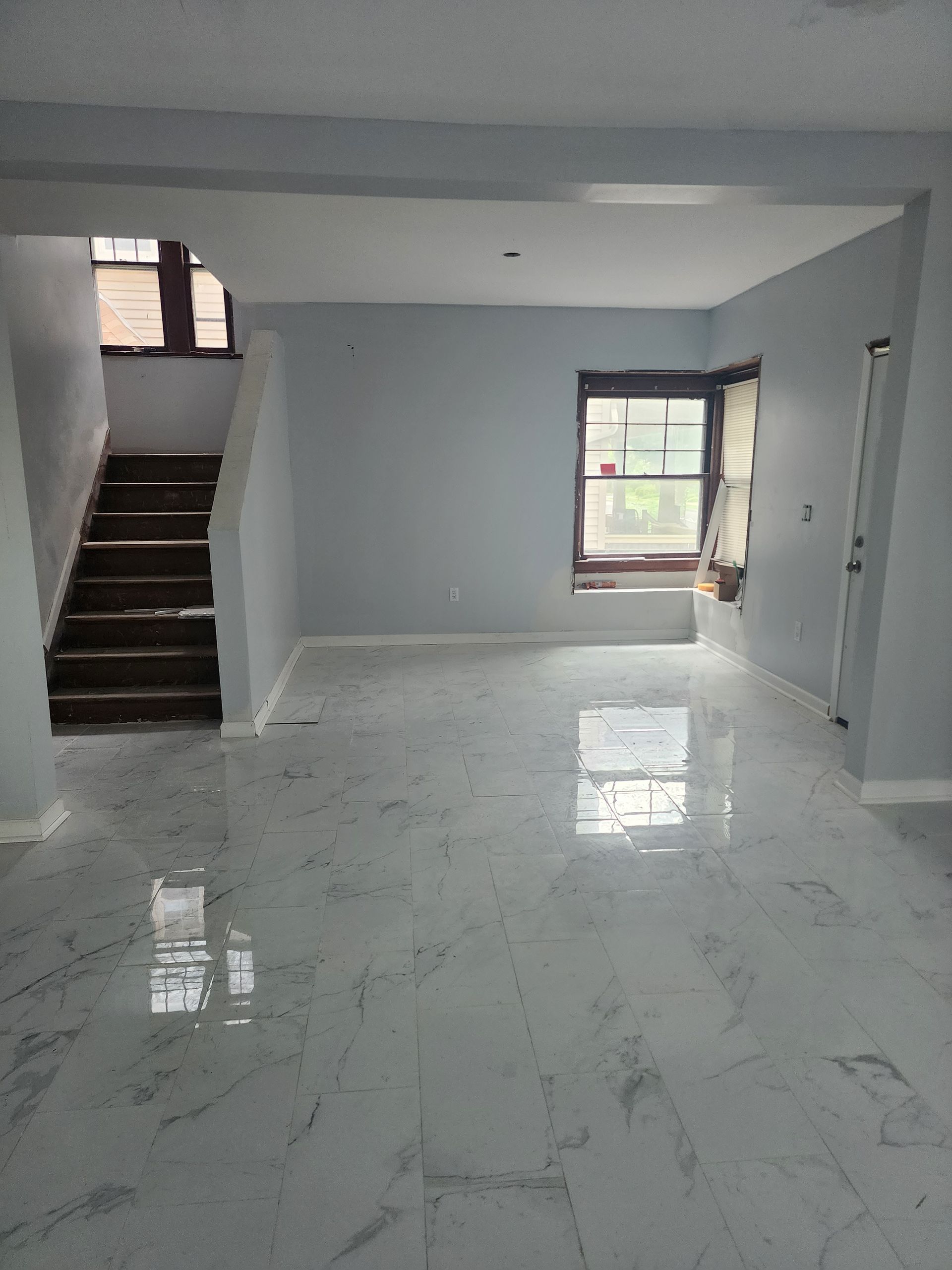 Empty modern living room with white marble floor, gray walls, stairs, and a window.
