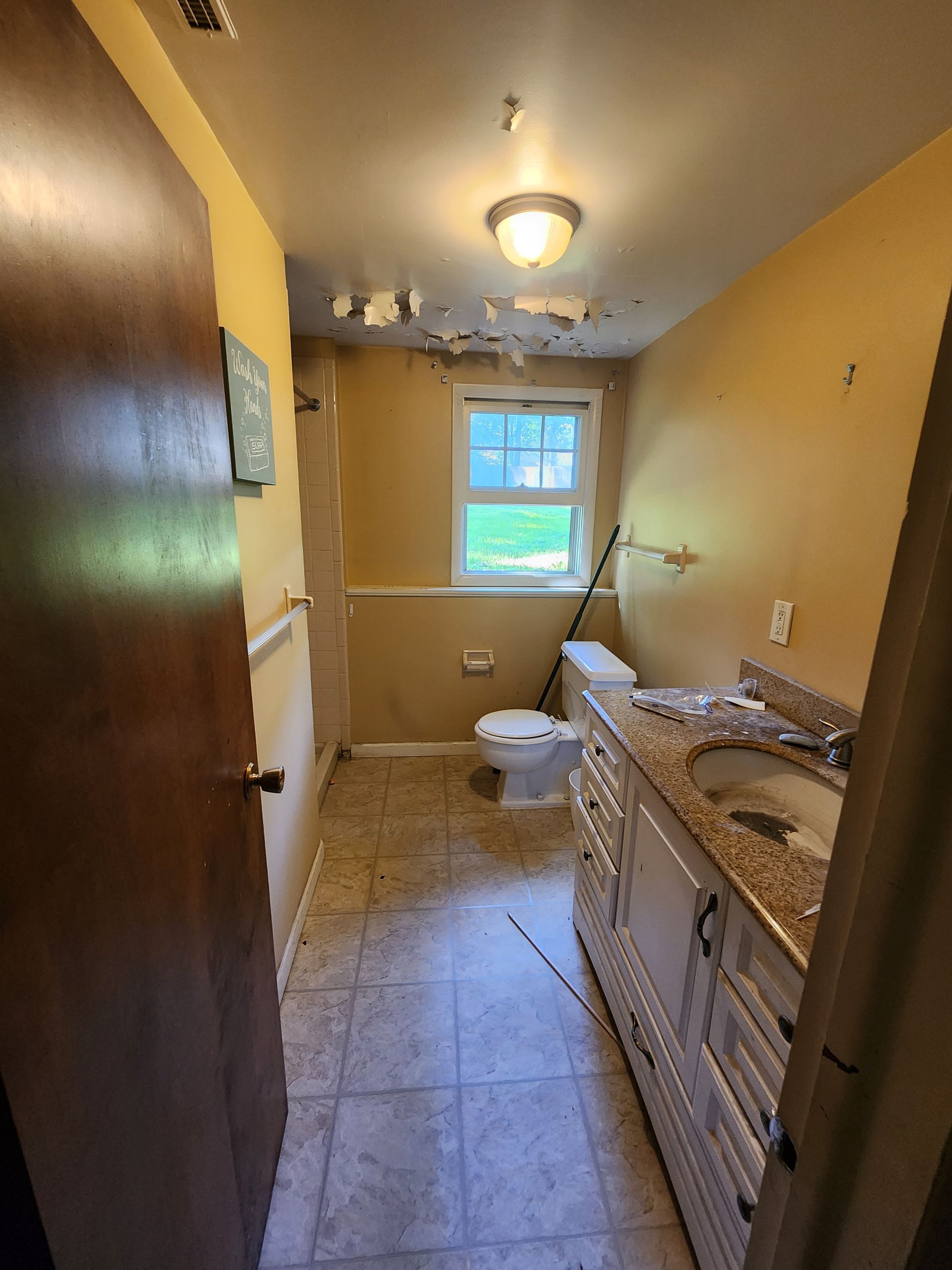 Narrow beige bathroom with tiled floor, sink vanity, toilet, window, and overhead light.