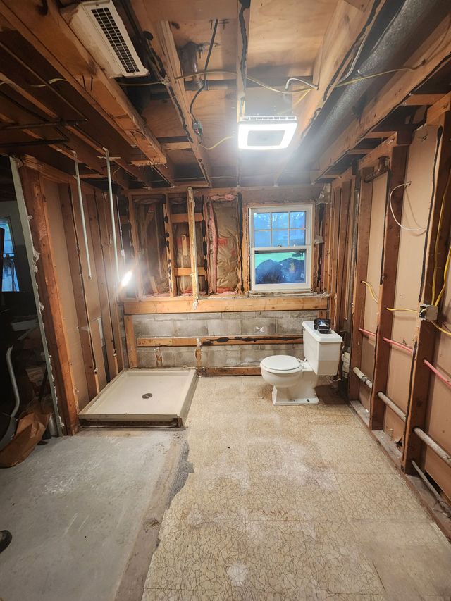 Renovated room with exposed studs, overhead lights, a small window, and a toilet on the floor.