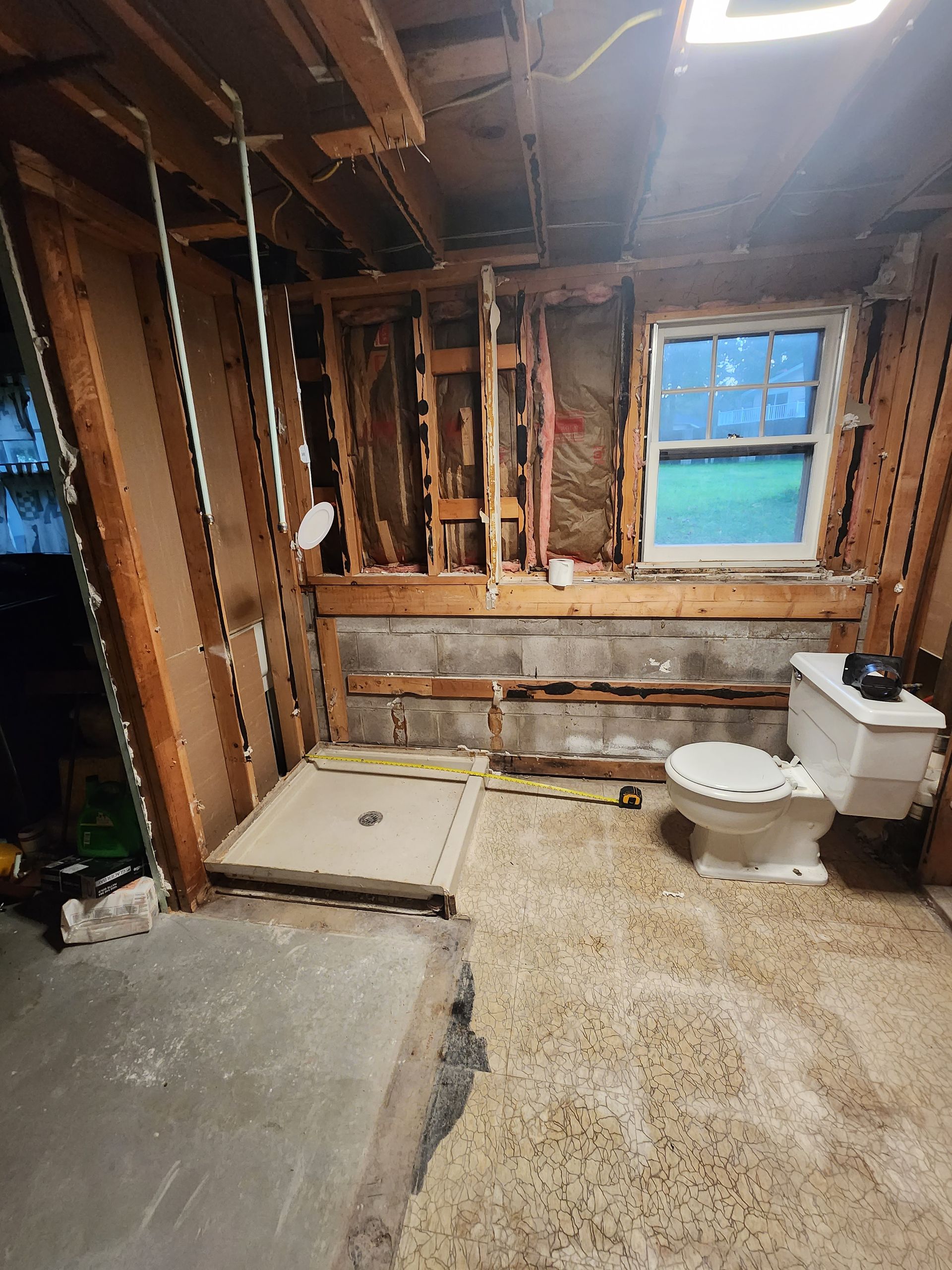Partially renovated bathroom with exposed studs, shower base, toilet, and a window