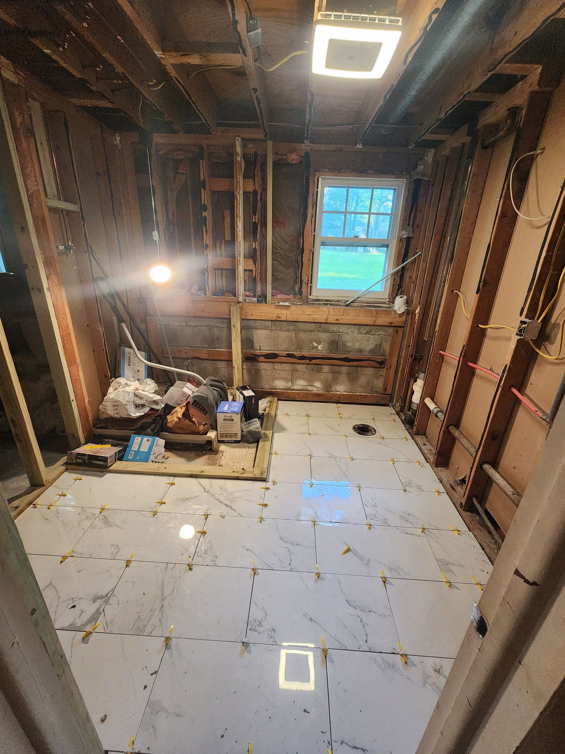 Partially renovated room with exposed studs, a bright work light, and a single blue window at the back.