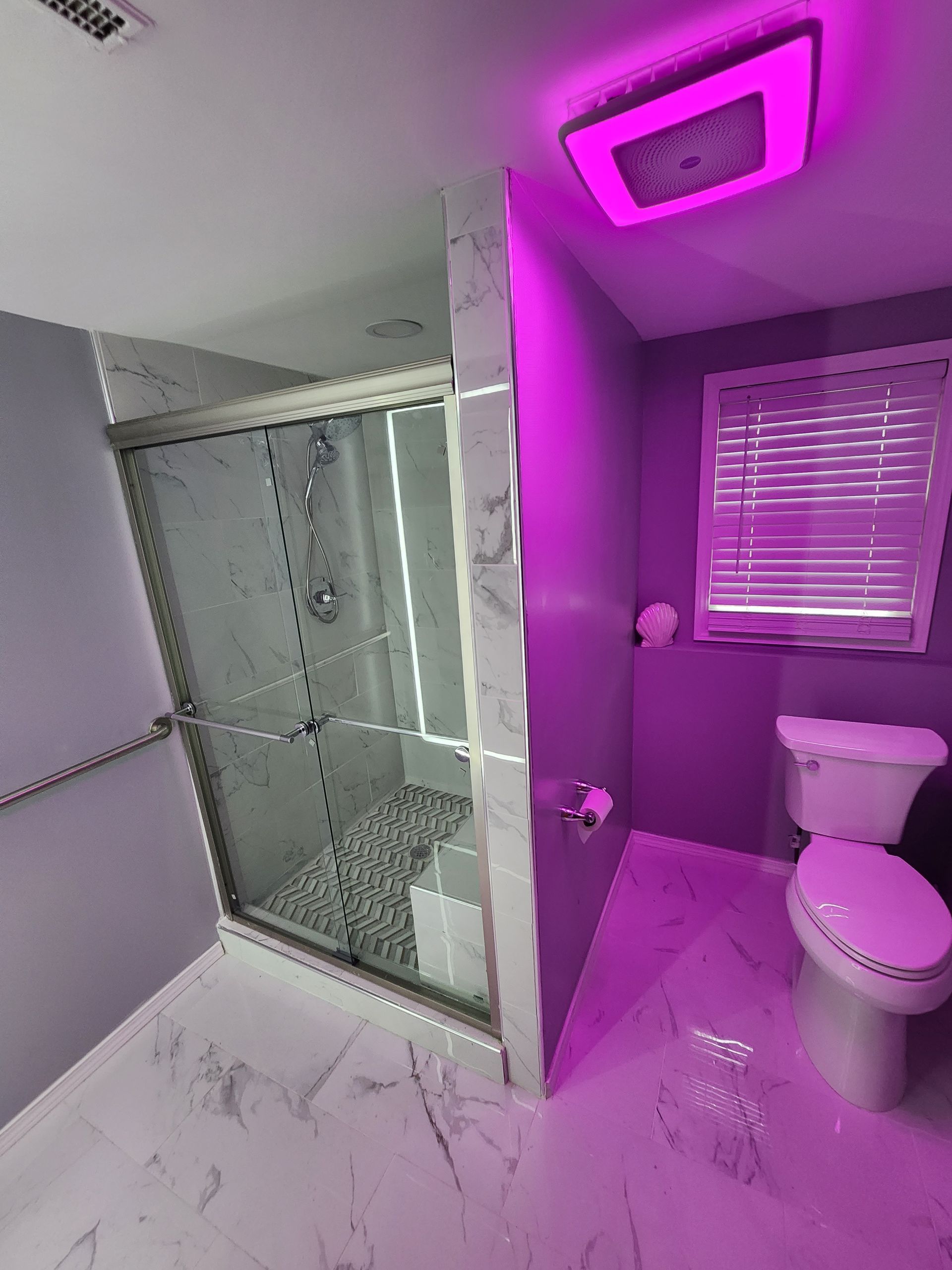 Modern bathroom with glass shower, toilet, and purple LED ceiling light