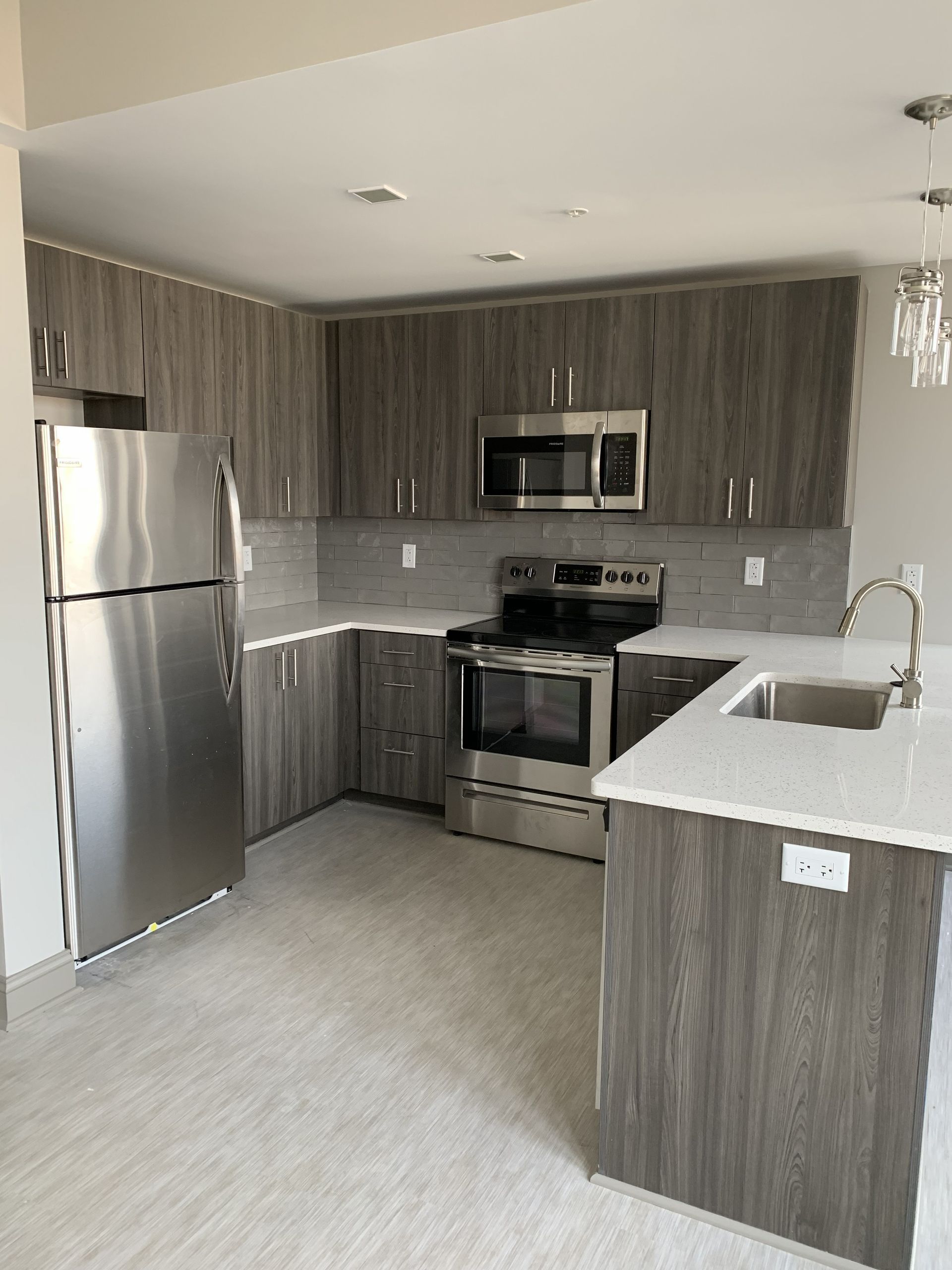 Modern kitchen with stainless steel appliances, gray cabinets, and a white countertop peninsula.