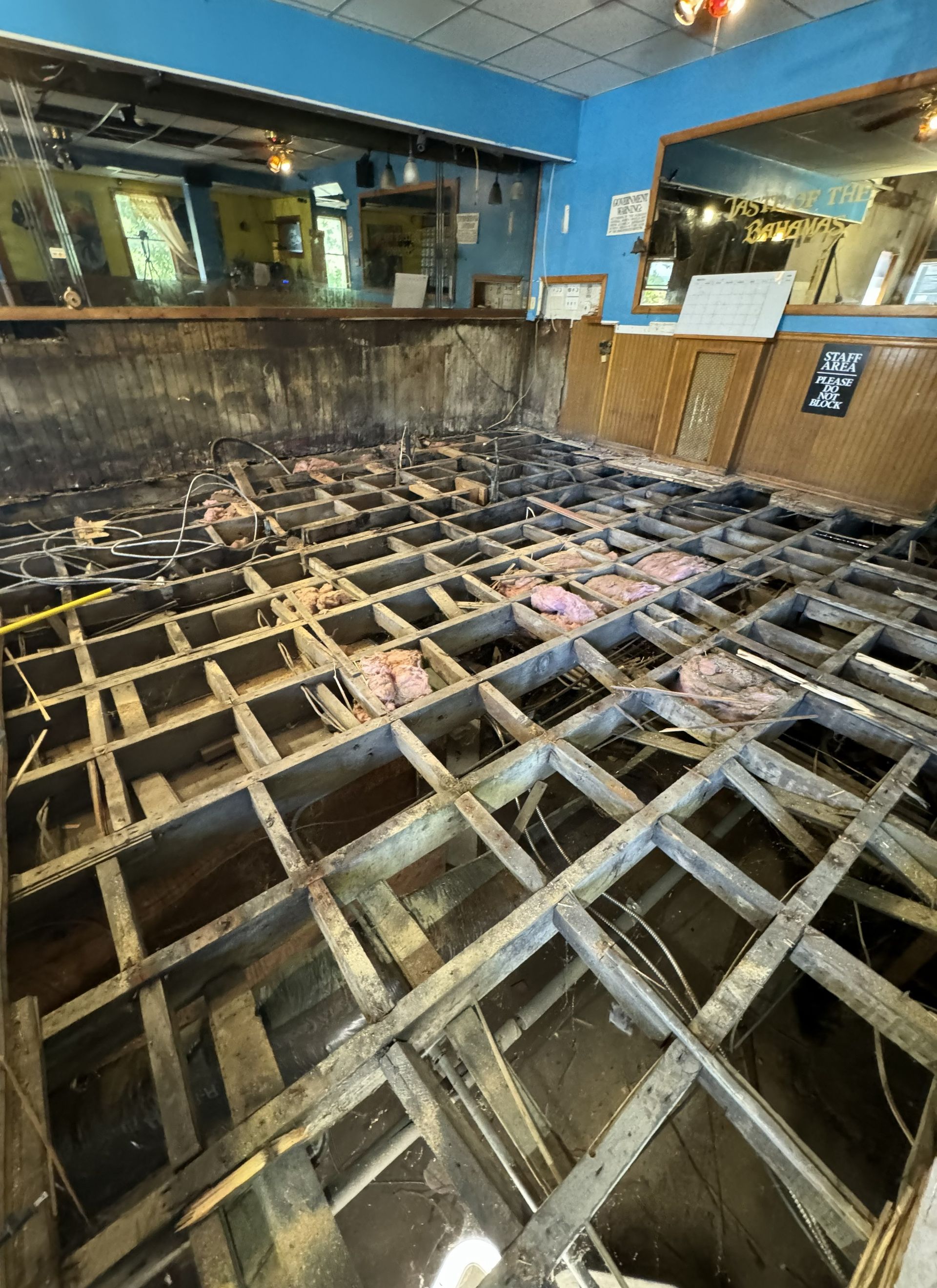 Partially demolished restaurant floor with exposed wooden joists and debris near a bar counter