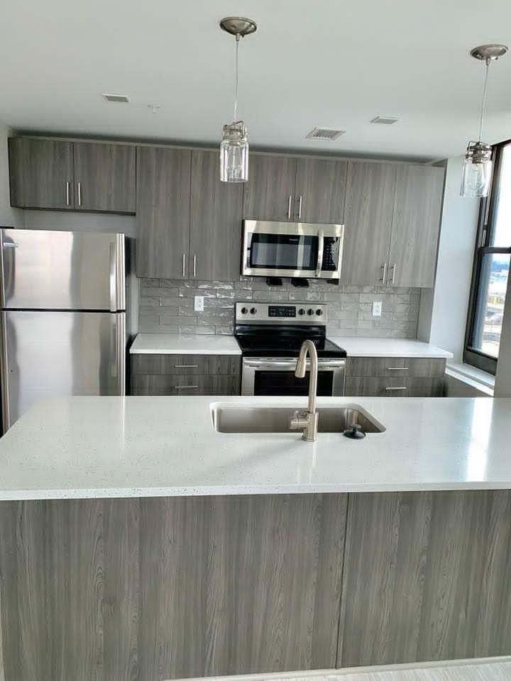 Modern kitchen with gray cabinets, stainless steel appliances, and a large white island with sink