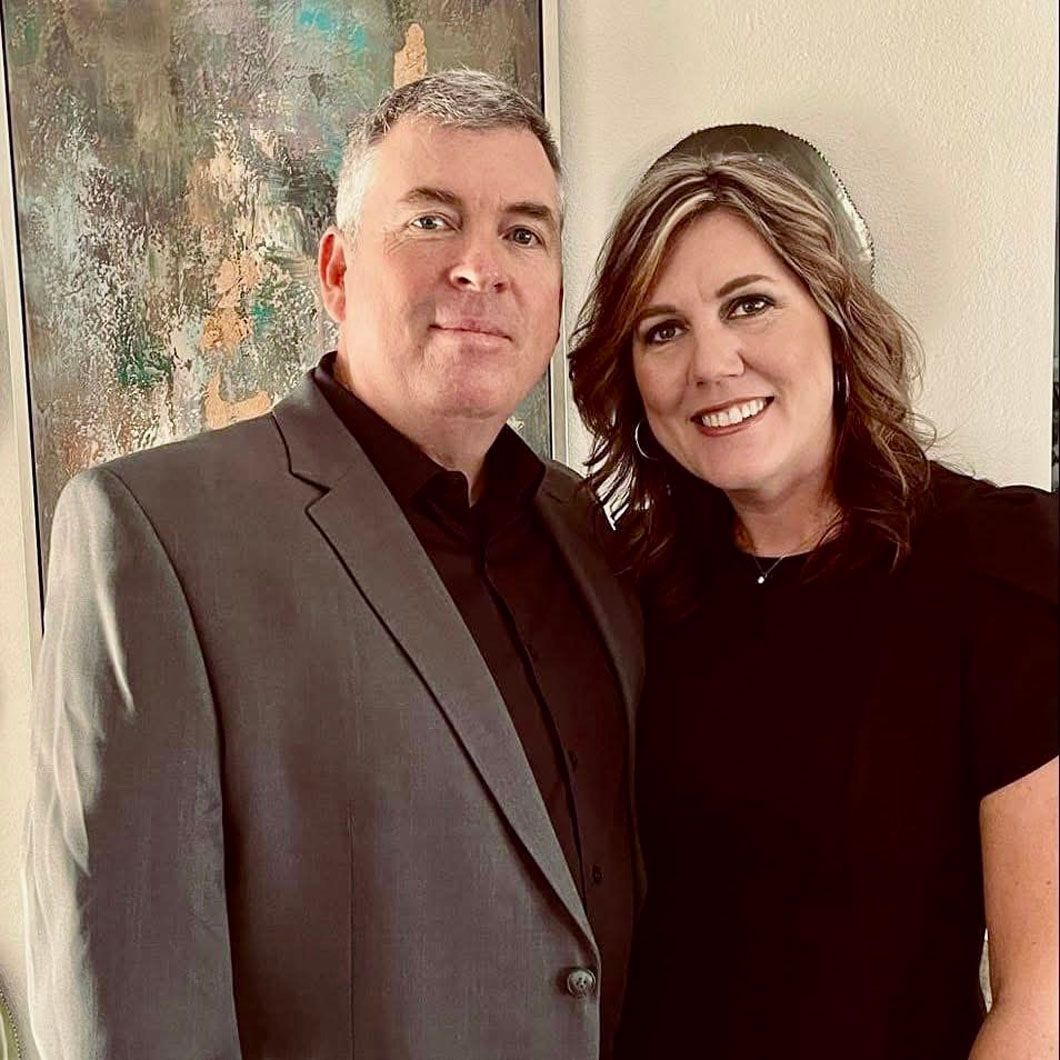 A man in a suit and a woman in a black shirt are posing for a picture.
