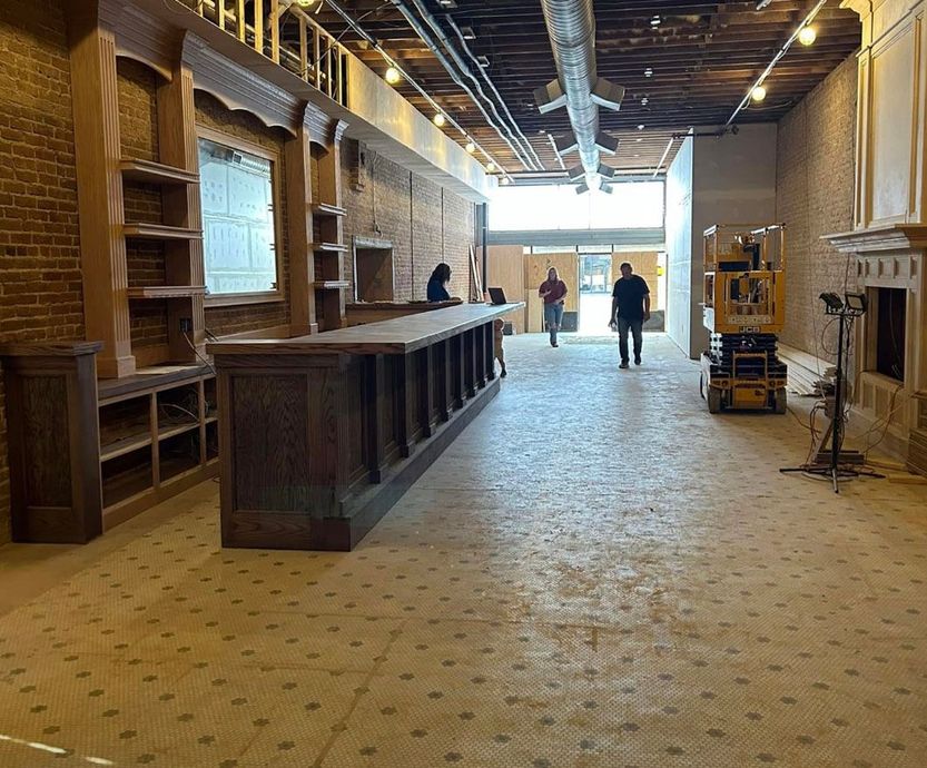 A group of people are standing in a large room with a long wooden bar.