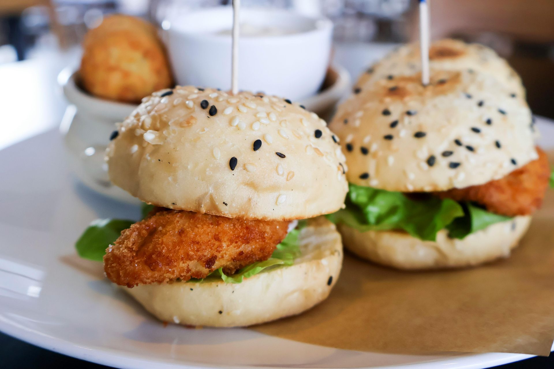 Two chicken sliders on a white plate with toothpicks in them.