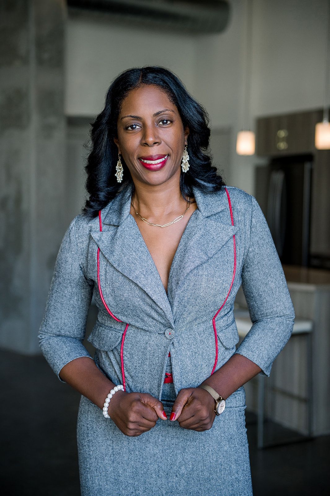 A woman in a gray suit and red earrings is standing in a room.