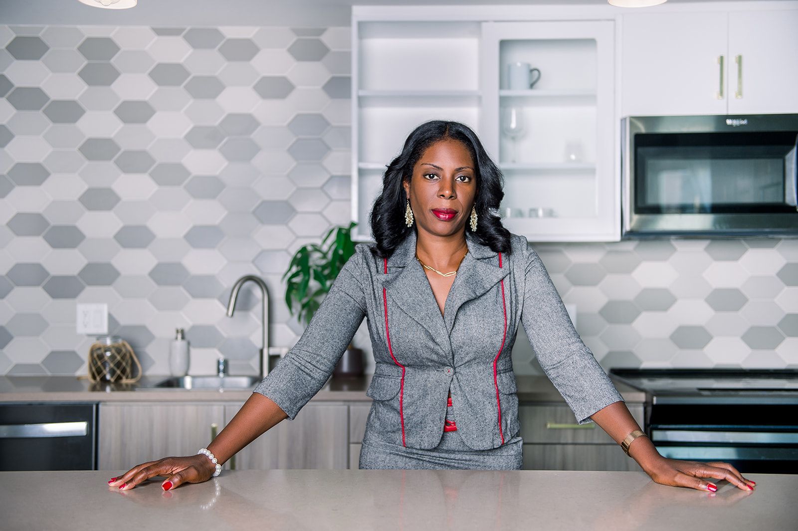 A woman in a suit is leaning on a counter in a kitchen.
