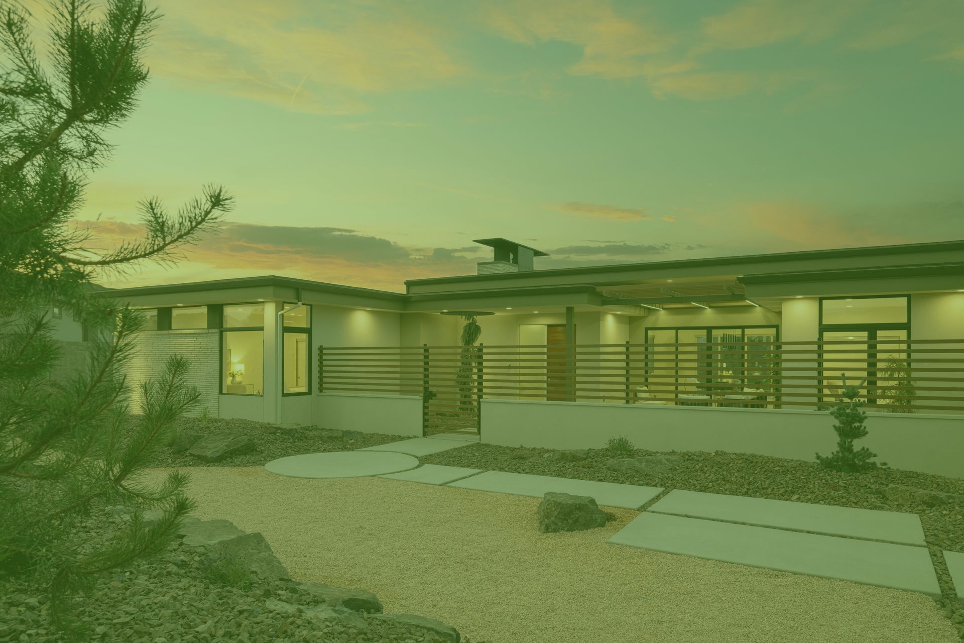 Modern single-story home with a light-colored facade, horizontal railings, and a gravel yard.