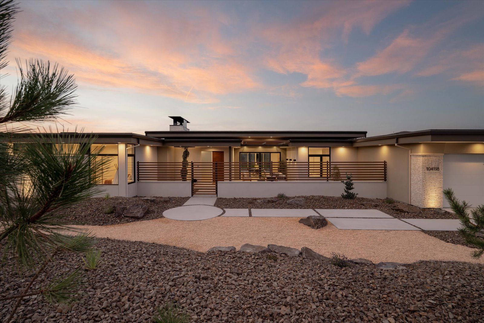 Modern single-story home with a wood fence, rock landscaping, and a sunset sky.