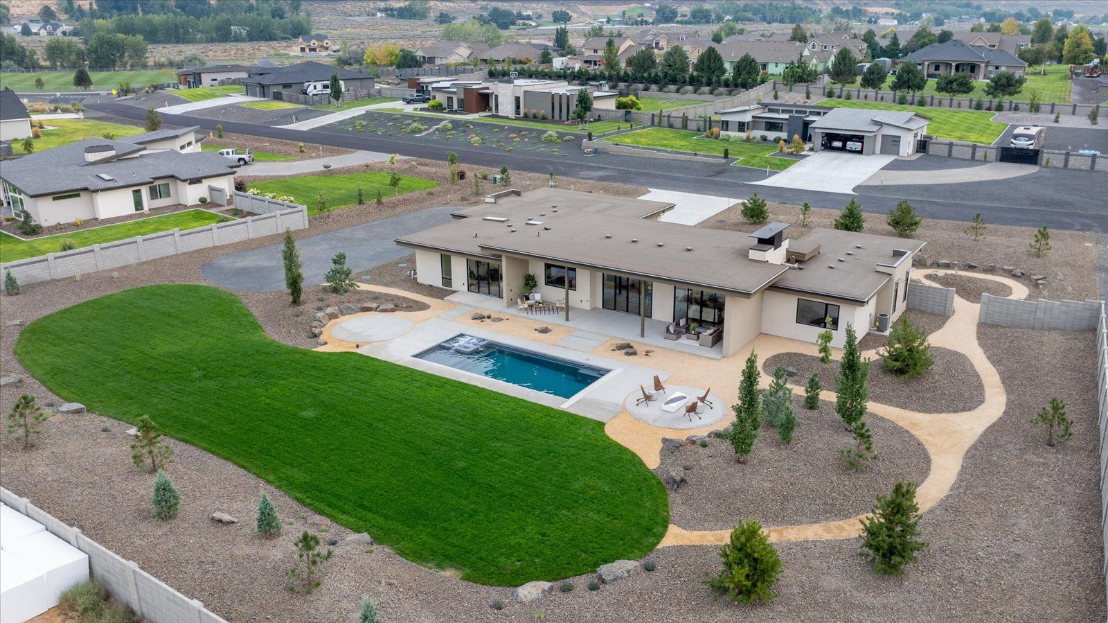 Aerial view of a modern house with a pool, green lawn, and gravel landscaping.