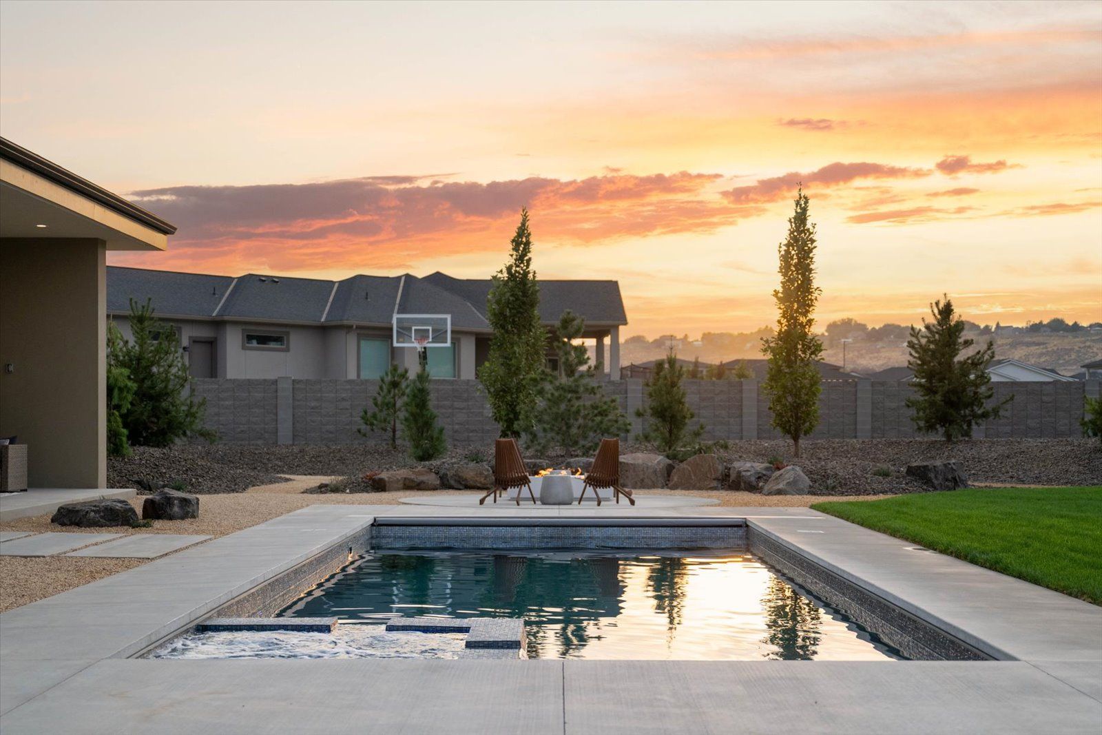 Rectangular pool with seating, landscaping, and colorful sunset.