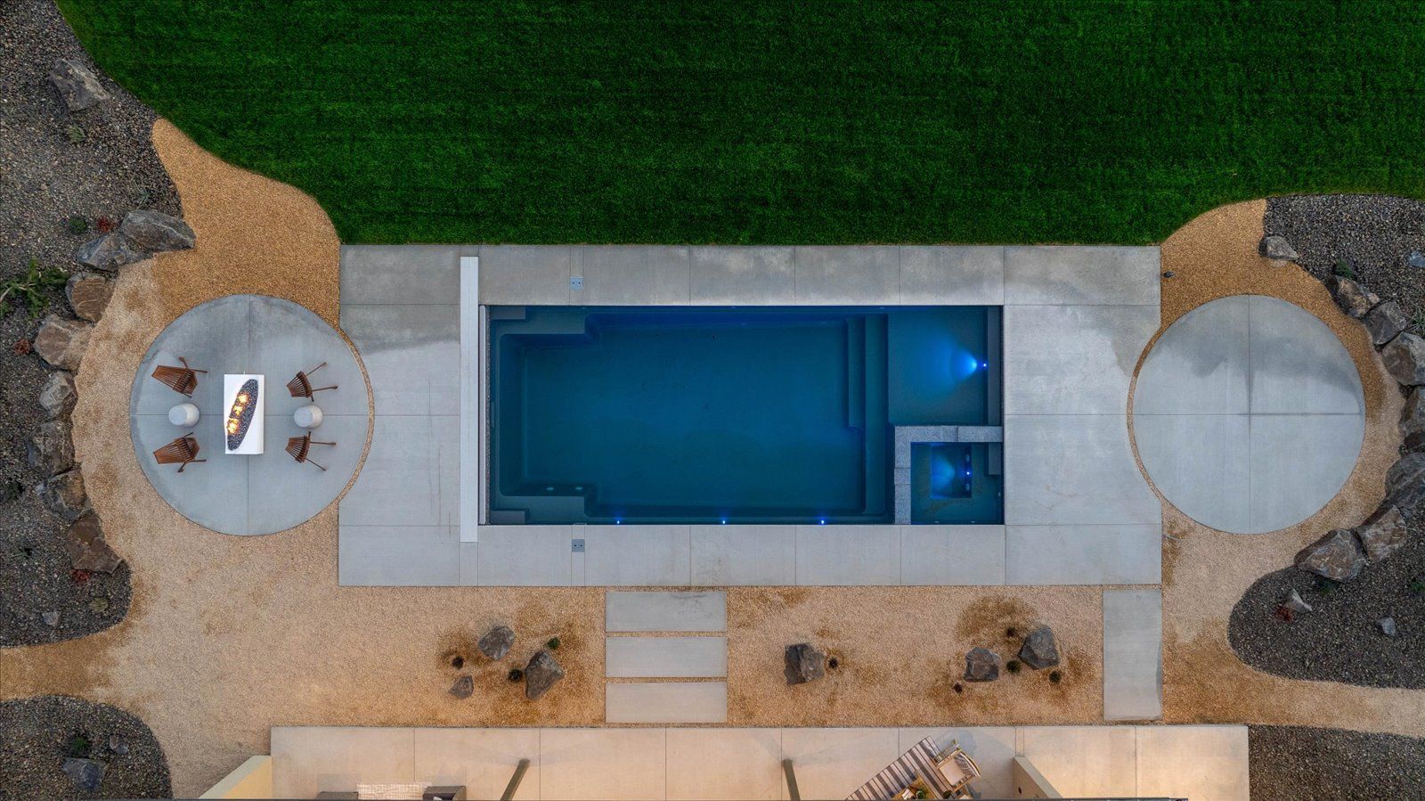 Overhead view of a rectangular pool with a jacuzzi, two circular patios, and landscaping with gravel and grass.