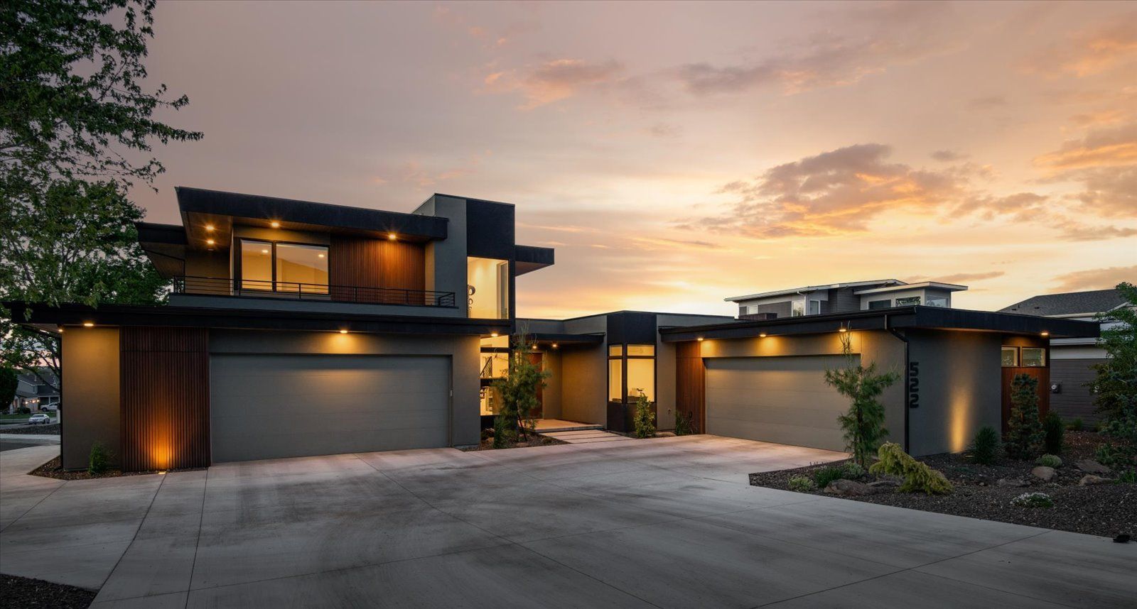 A modern house with two garages and a driveway at sunset.