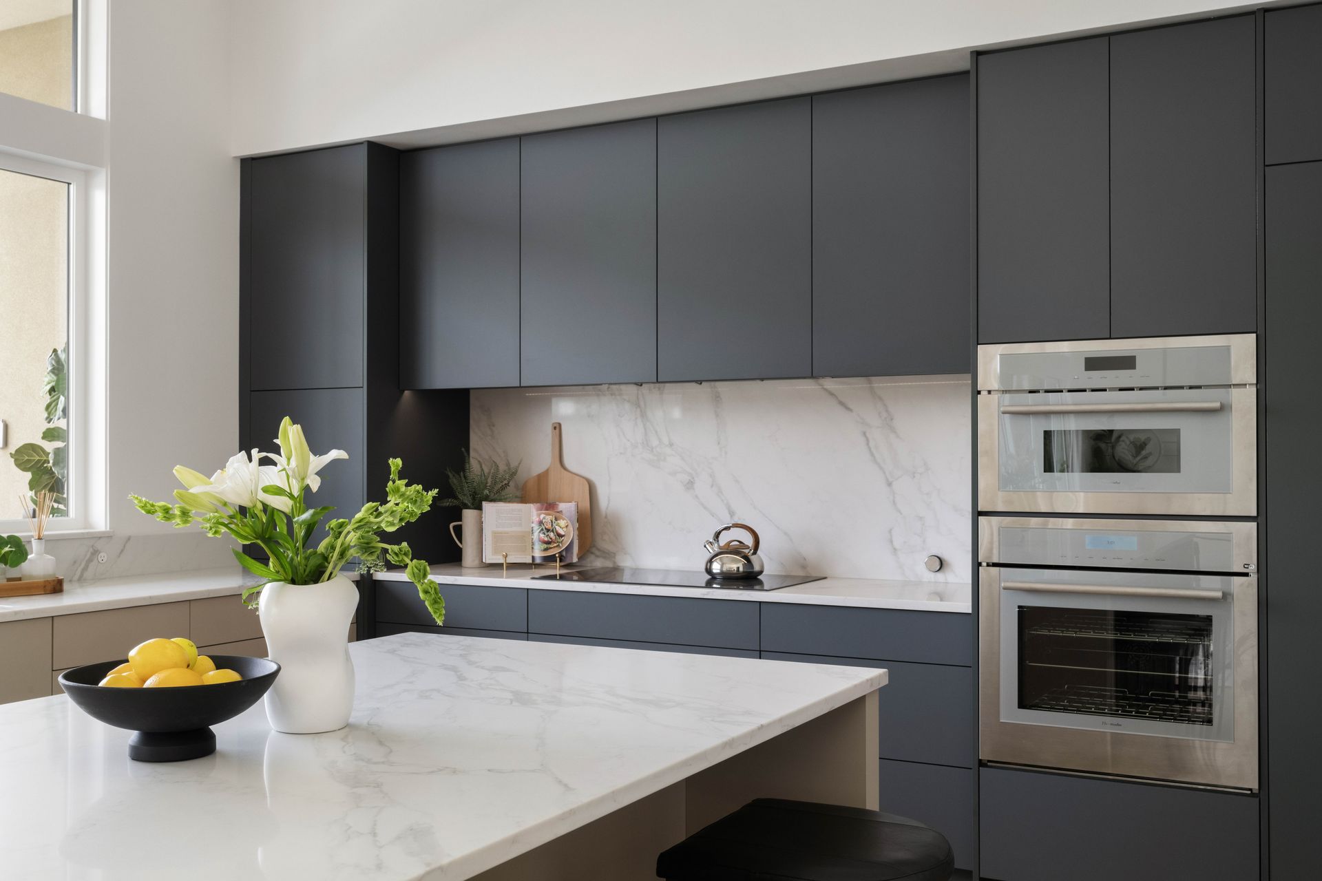 Modern kitchen with dark gray cabinets, white countertops, and stainless steel oven.