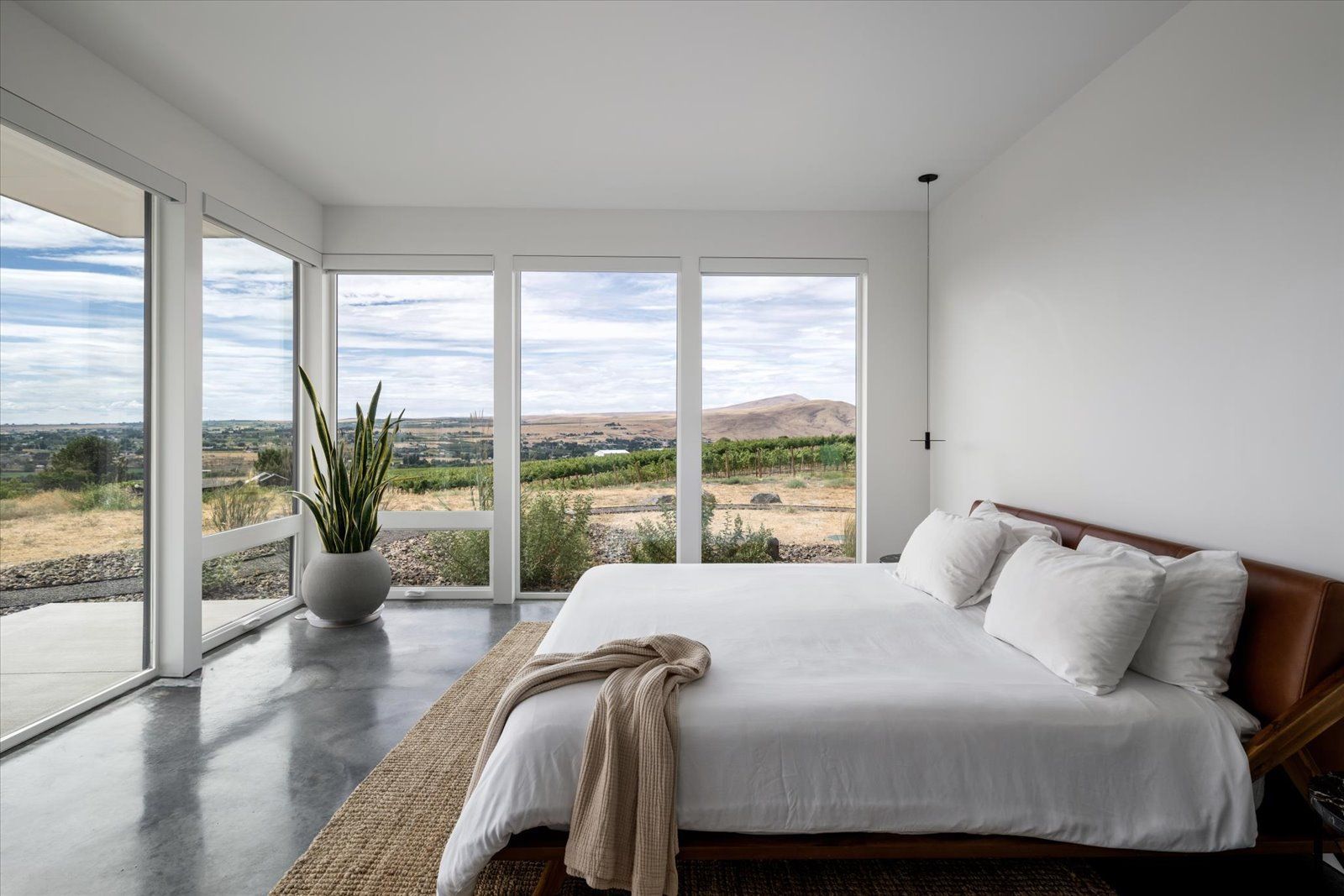 Bedroom with large windows overlooking a landscape, a bed with white linens, and a potted plant.