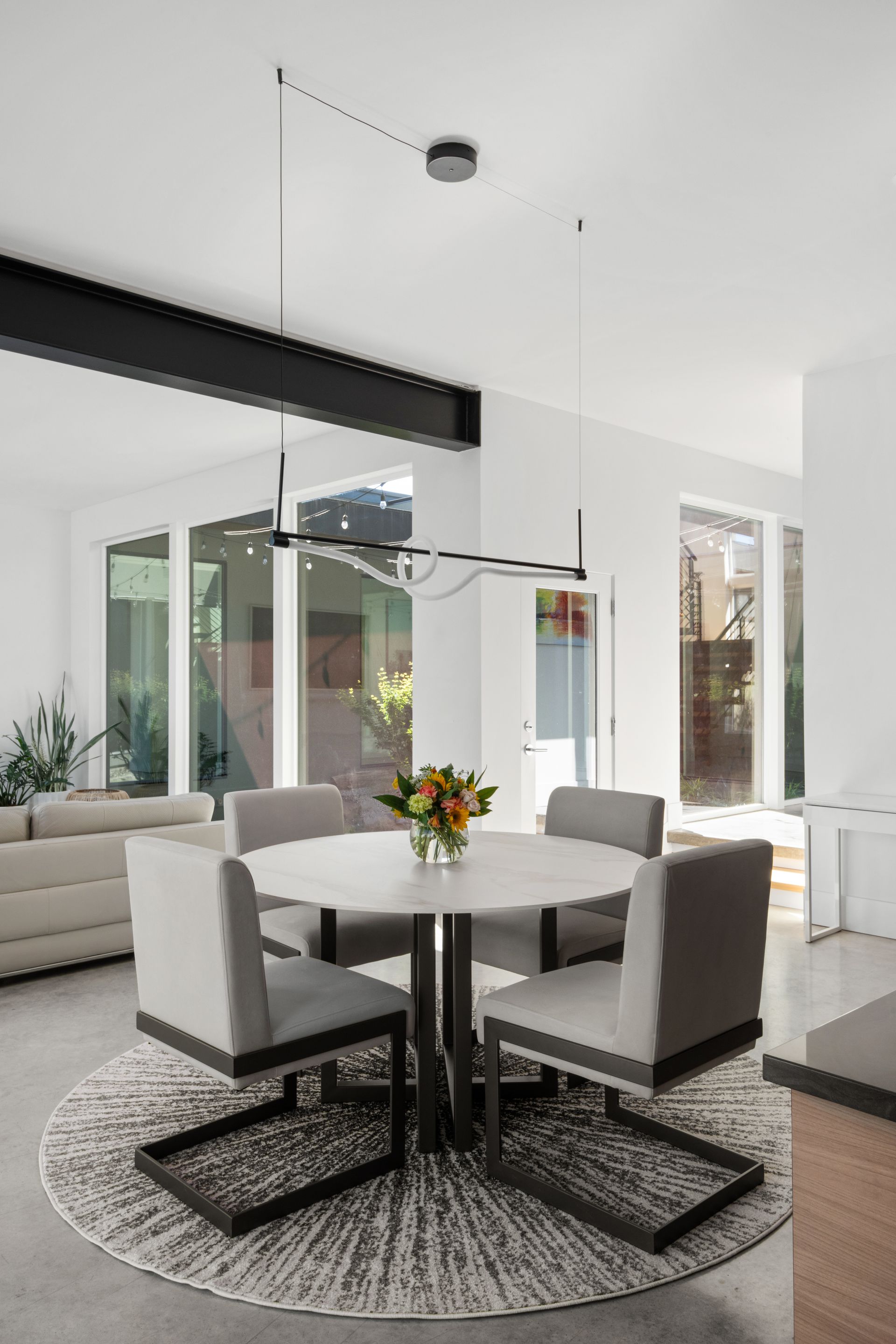 Modern dining area with round table, four chairs, and abstract rug, under a black light fixture.
