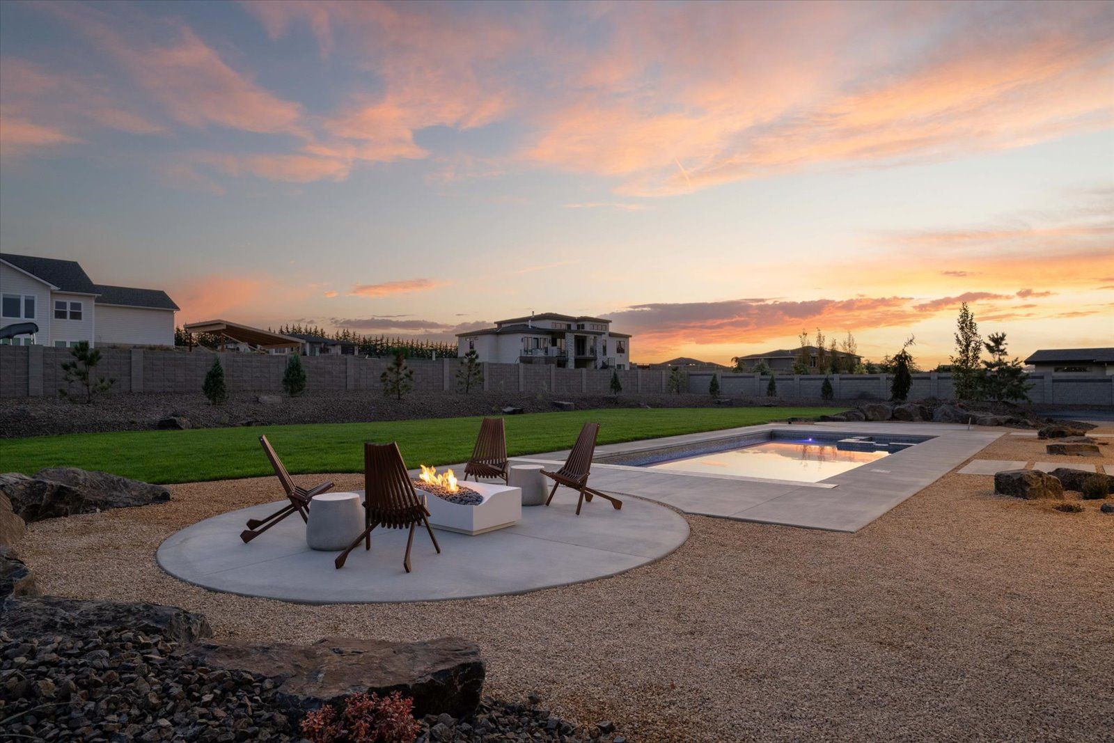 Backyard with pool, fire pit, gravel, and lawn at sunset.