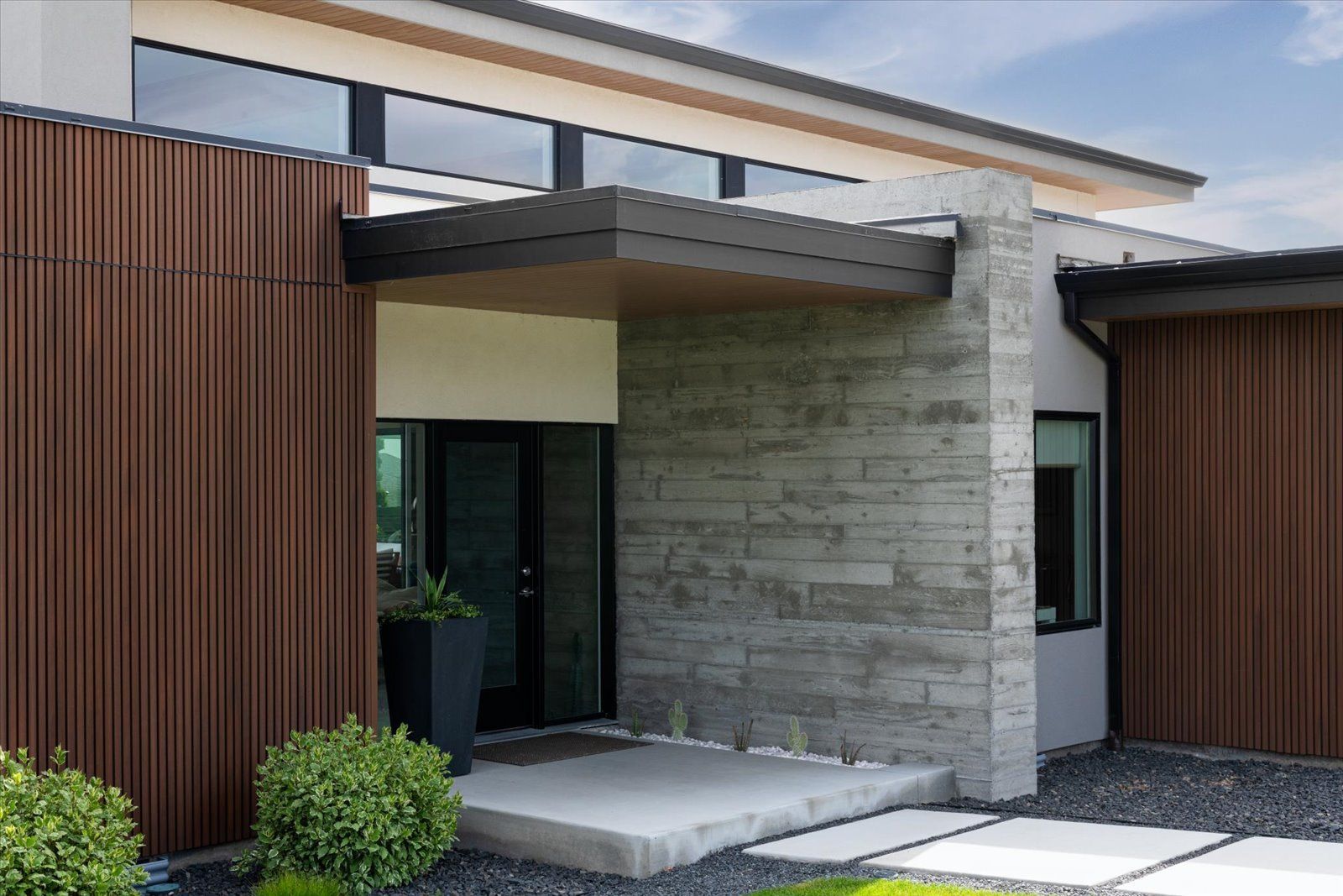 A modern house with a brick wall and a concrete walkway leading to the front door.