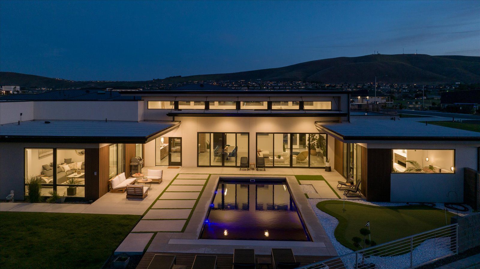 A modern house with a large swimming pool in the backyard at night.