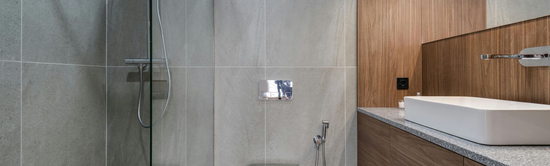 Modern bathroom with gray tiled shower and wood paneling, featuring a rectangular sink.