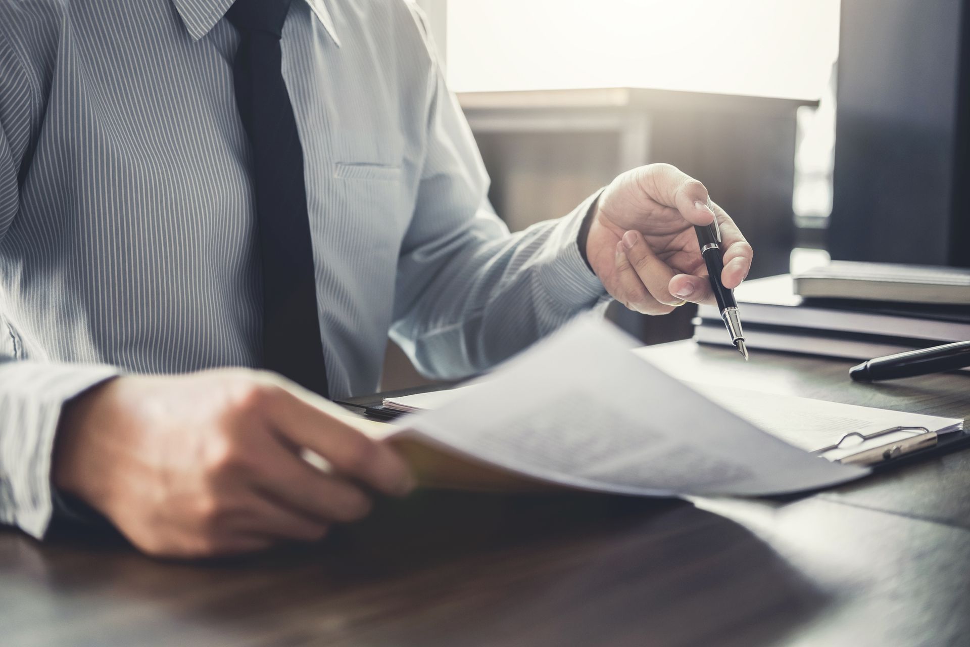 Man in a shirt and tie pointing at a document with a pen at a desk; focus on his hands.