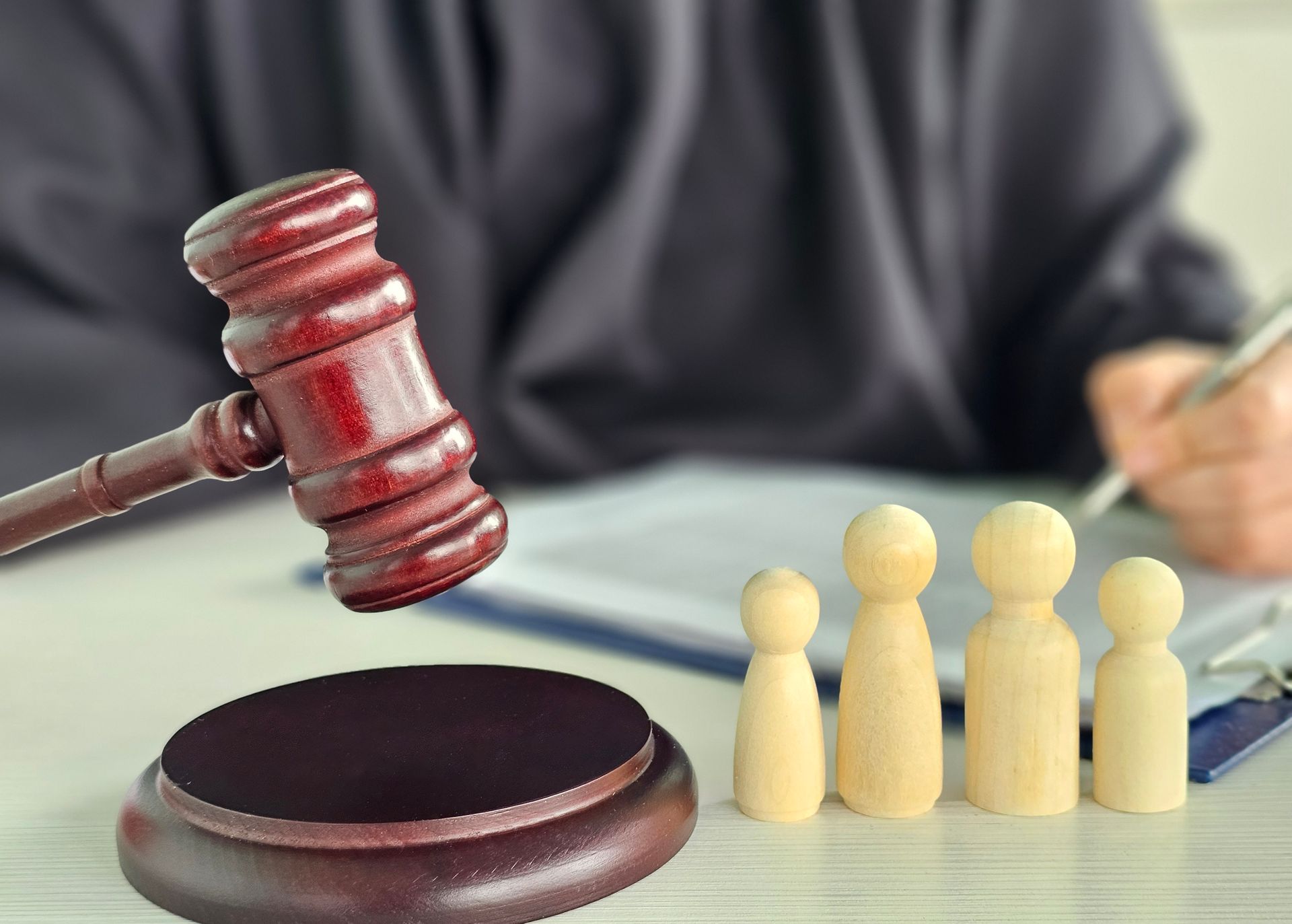 Wooden gavel beside figurines and clipboard in legal-themed setting.