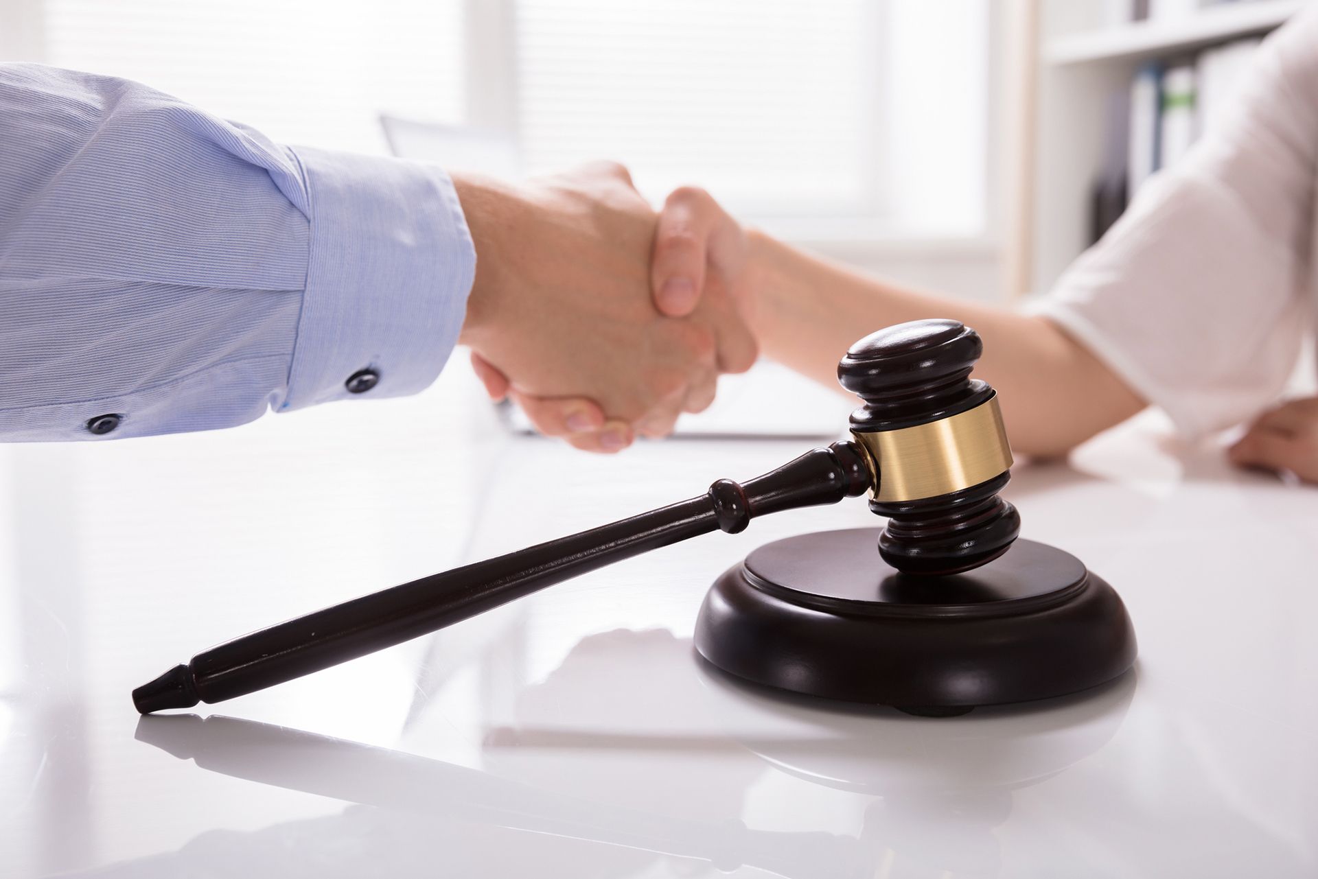 Handshake in legal office with judge’s gavel symbolizing law agreement or settlement. Handshake in legal office with judge’s gavel symbolizing law agreement or settlement.