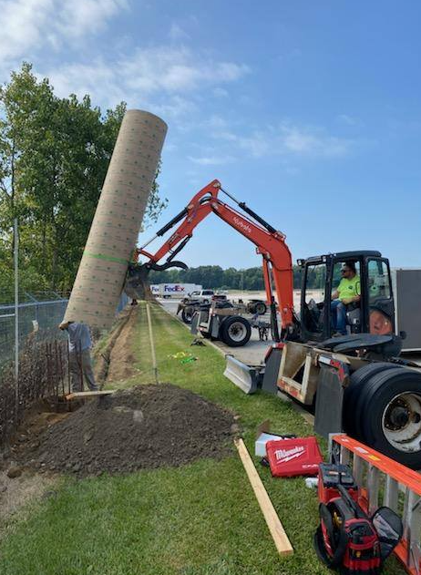 Six men posing in front of a company logo. They wear work clothes in a workshop setting. Six men posing in front of a company logo. They wear work clothes in a workshop setting.