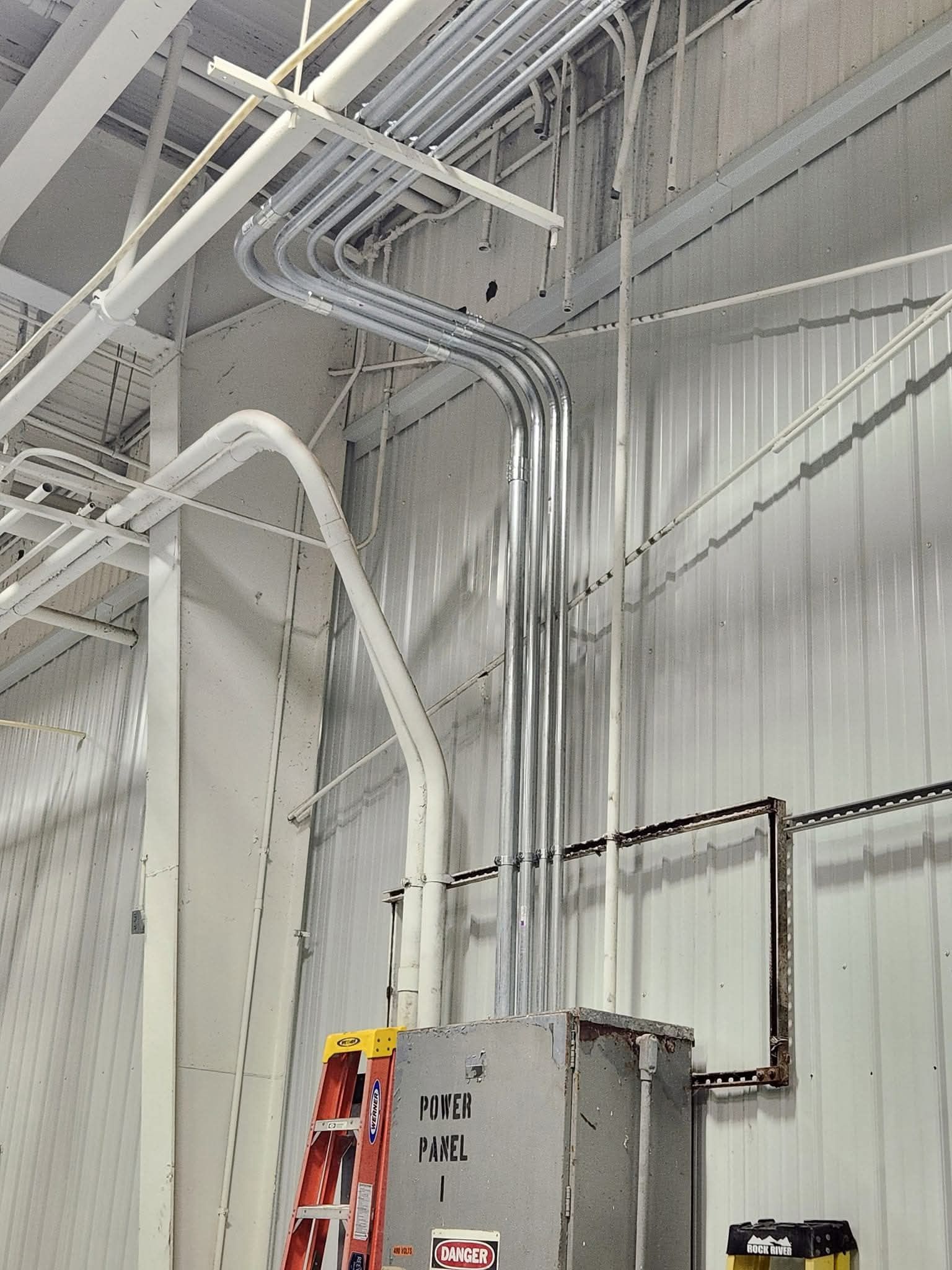 Industrial interior with pipes, lights, and yellow beams against a dark ceiling.